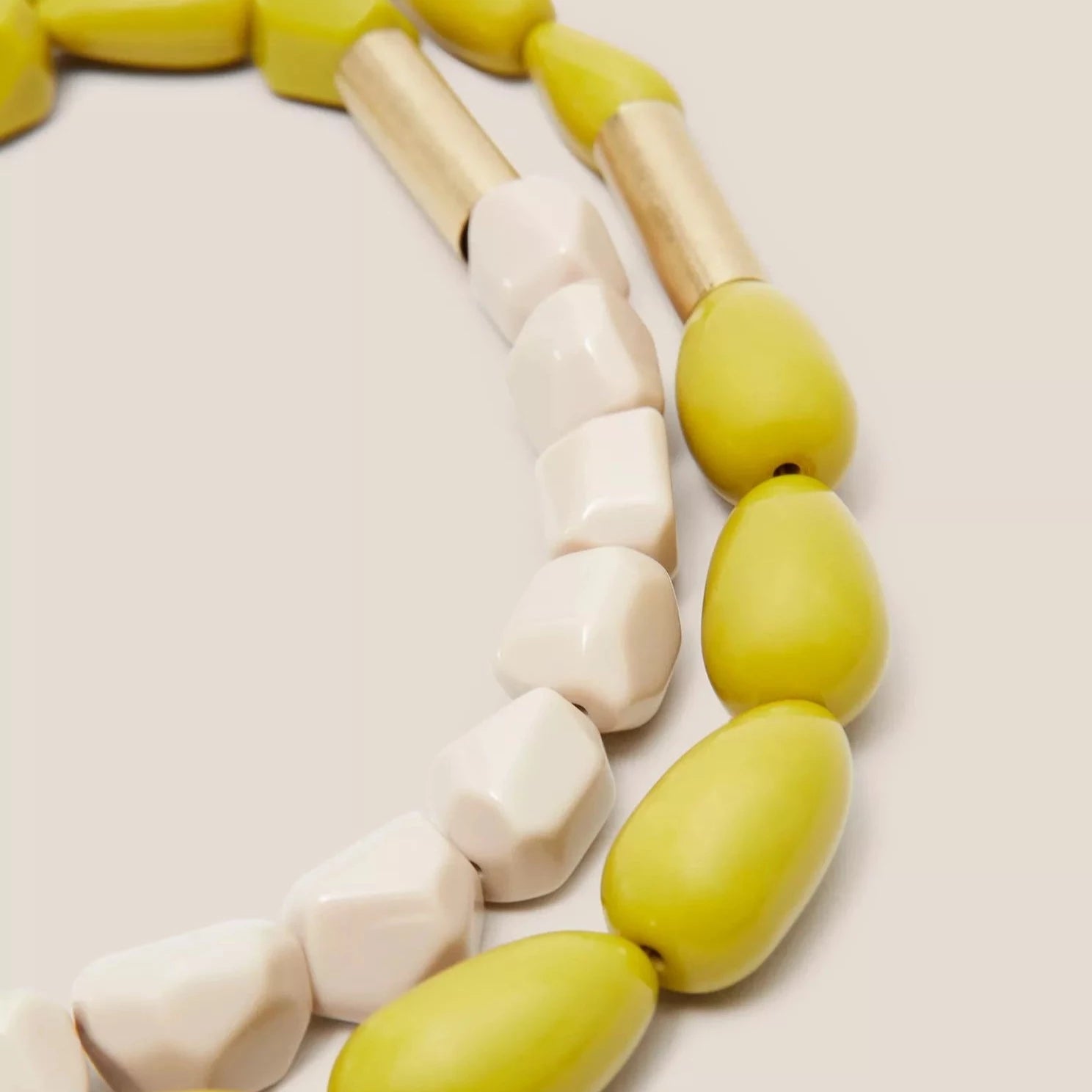 Statement necklace with large, faceted off-white and mustard yellow beads separated by gold-toned spacers.