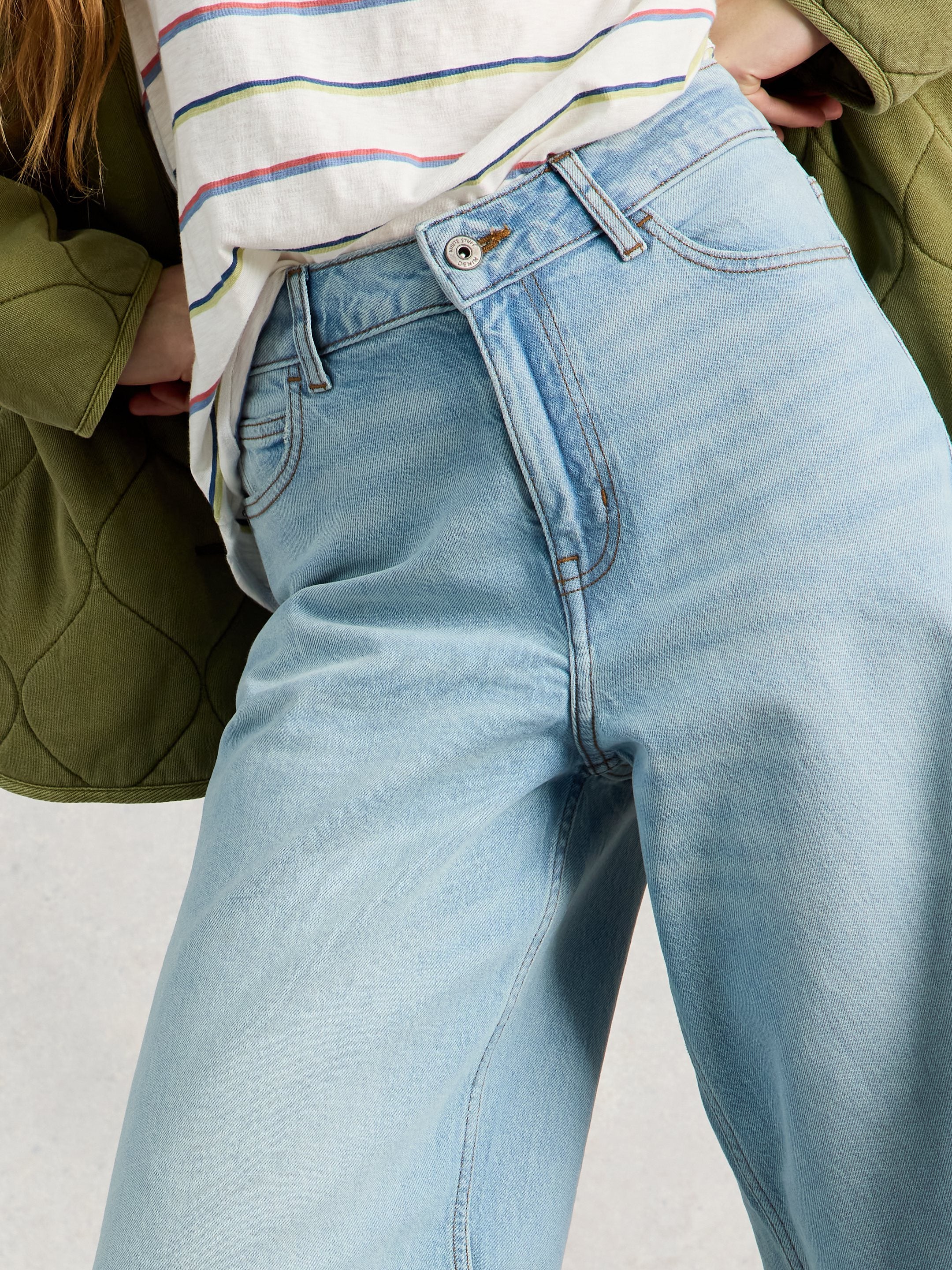 Light blue jeans worn by a person with a green jacket and striped shirt on a light gray background
