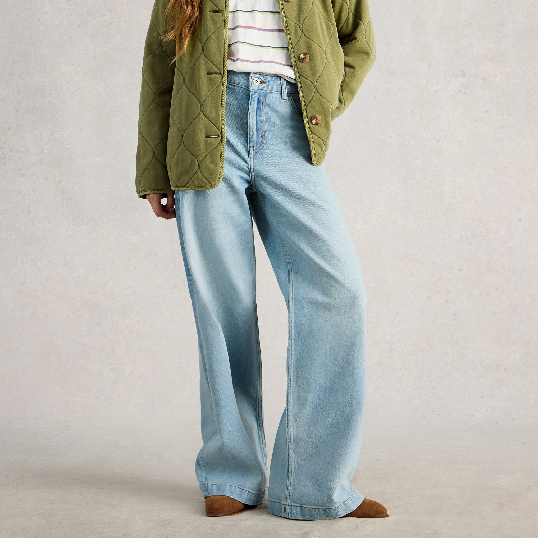 Person wearing light blue jeans and a green jacket on a plain background