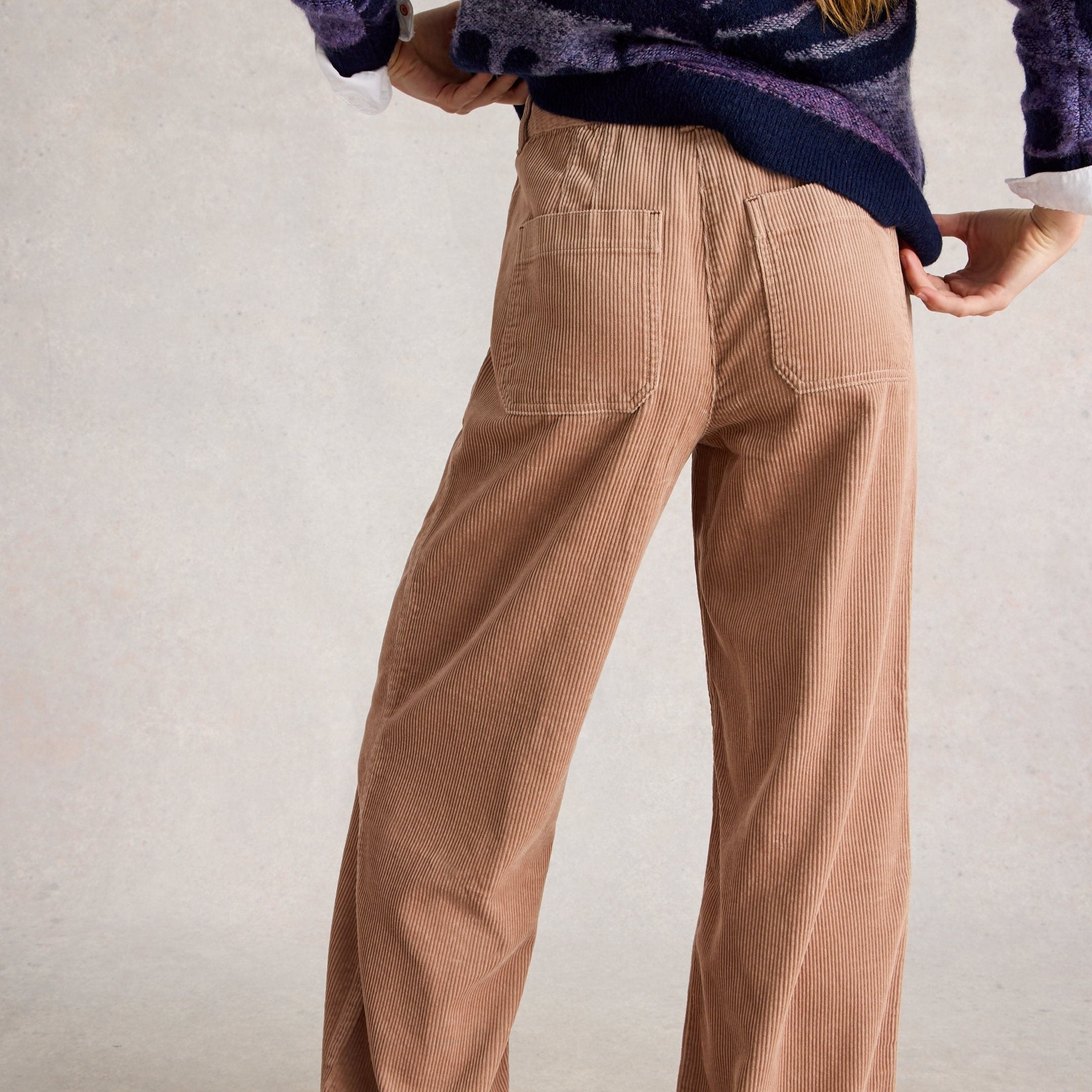 Person wearing brown wide-leg pants and a purple sweater on a plain background
