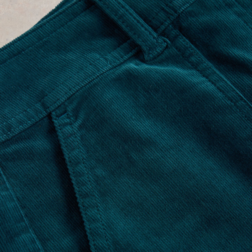 Close-up of teal corduroy fabric, showing texture and stitching detail of a garment's waistband and pocket.