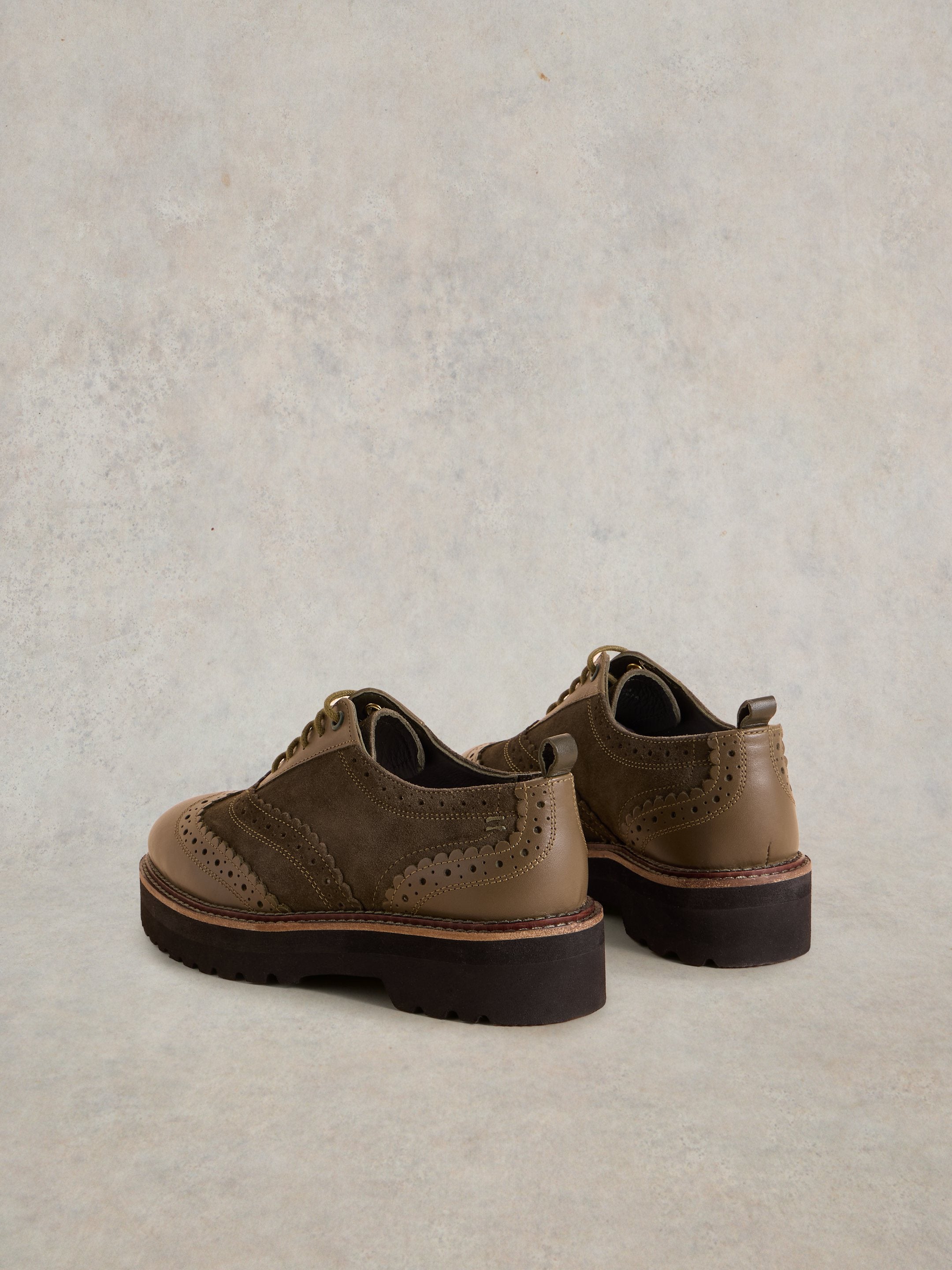 Pair of olive-green leather brogue shoes with platform soles and decorative stitching.