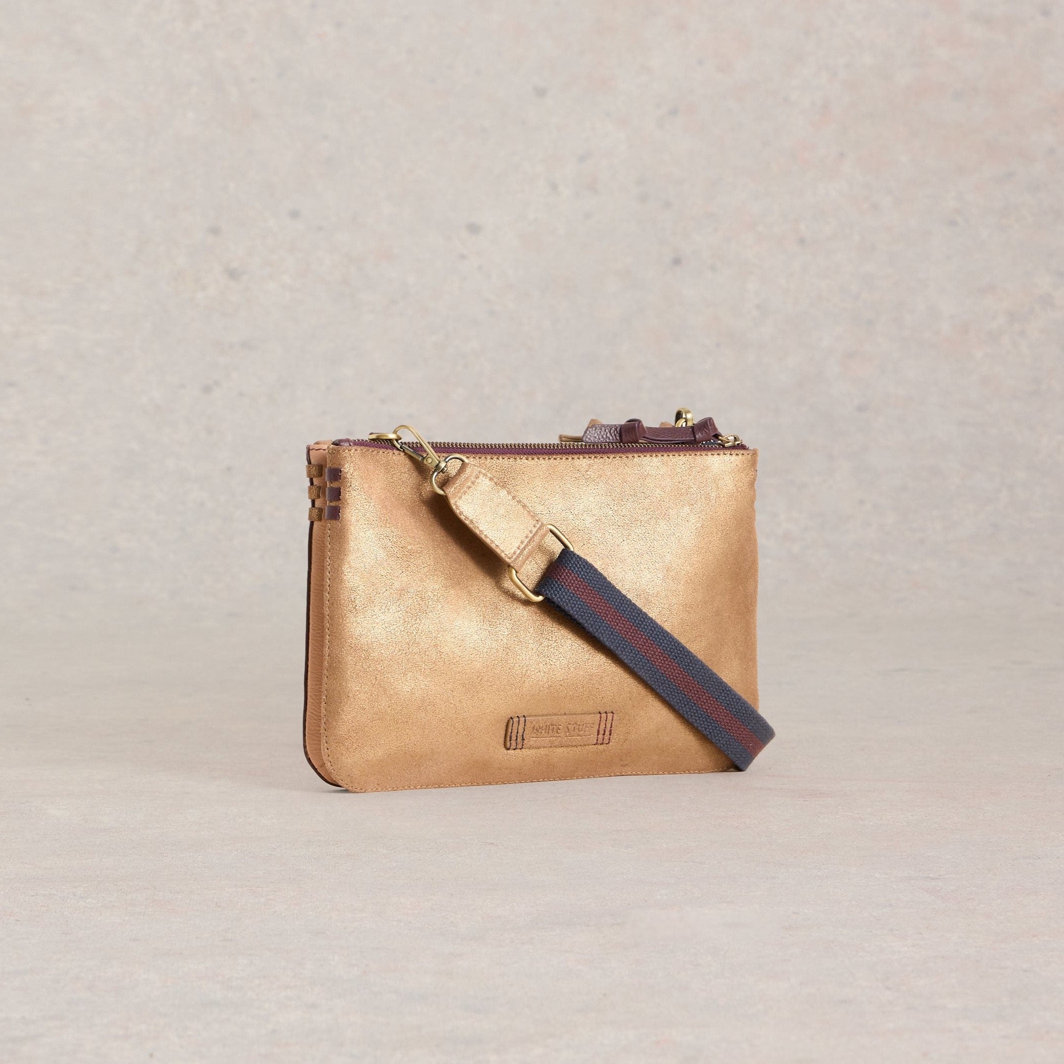 Gold metallic leather crossbody bag with a dark navy and burgundy striped shoulder strap and a top zip closure.