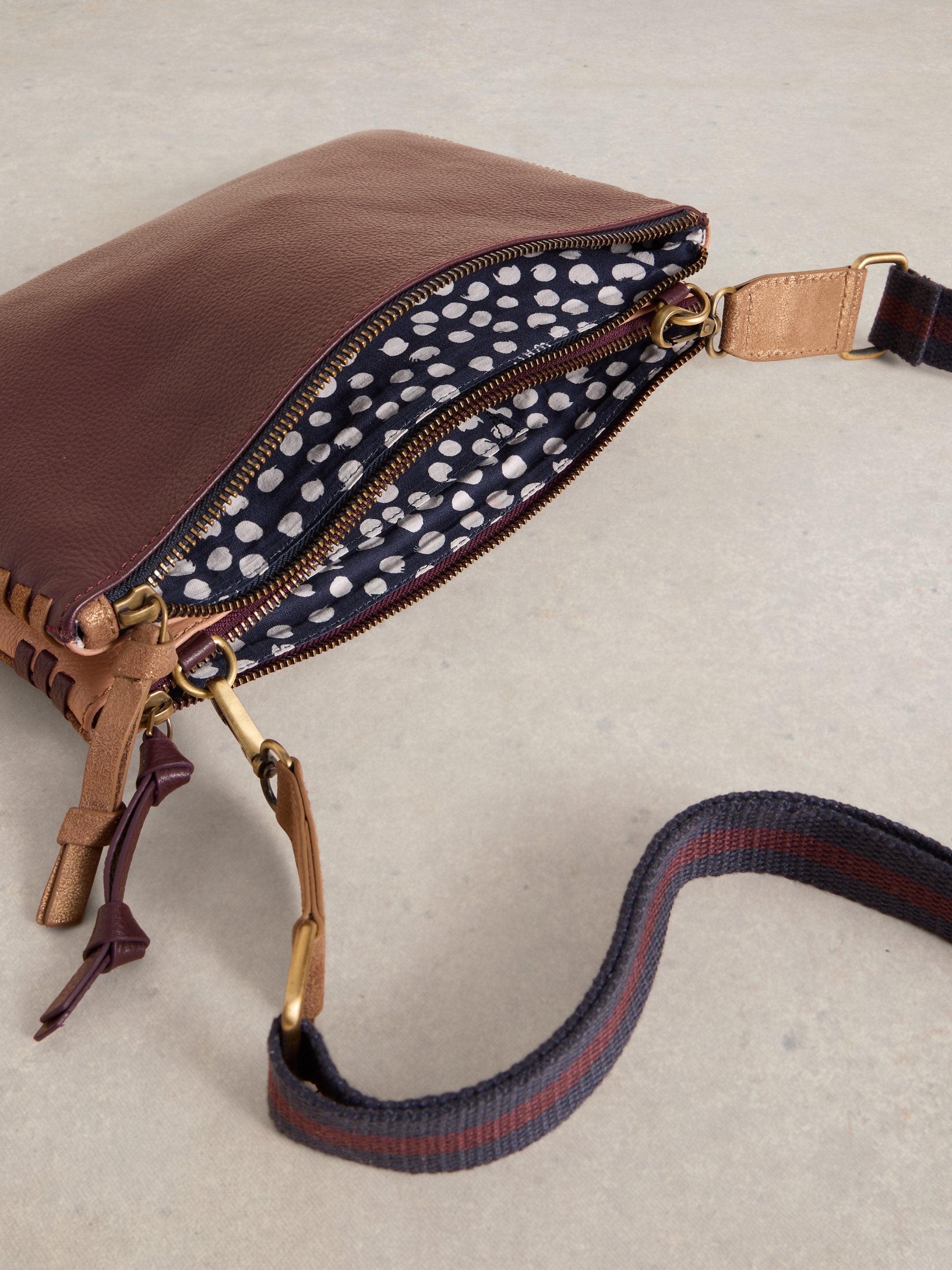 Burgundy leather crossbody bag with two zippered compartments, a patterned interior, and an adjustable strap.