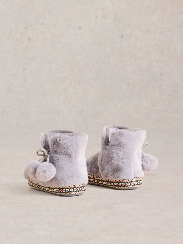 Pair of gray faux fur slipper boots with pom-poms and patterned trim.