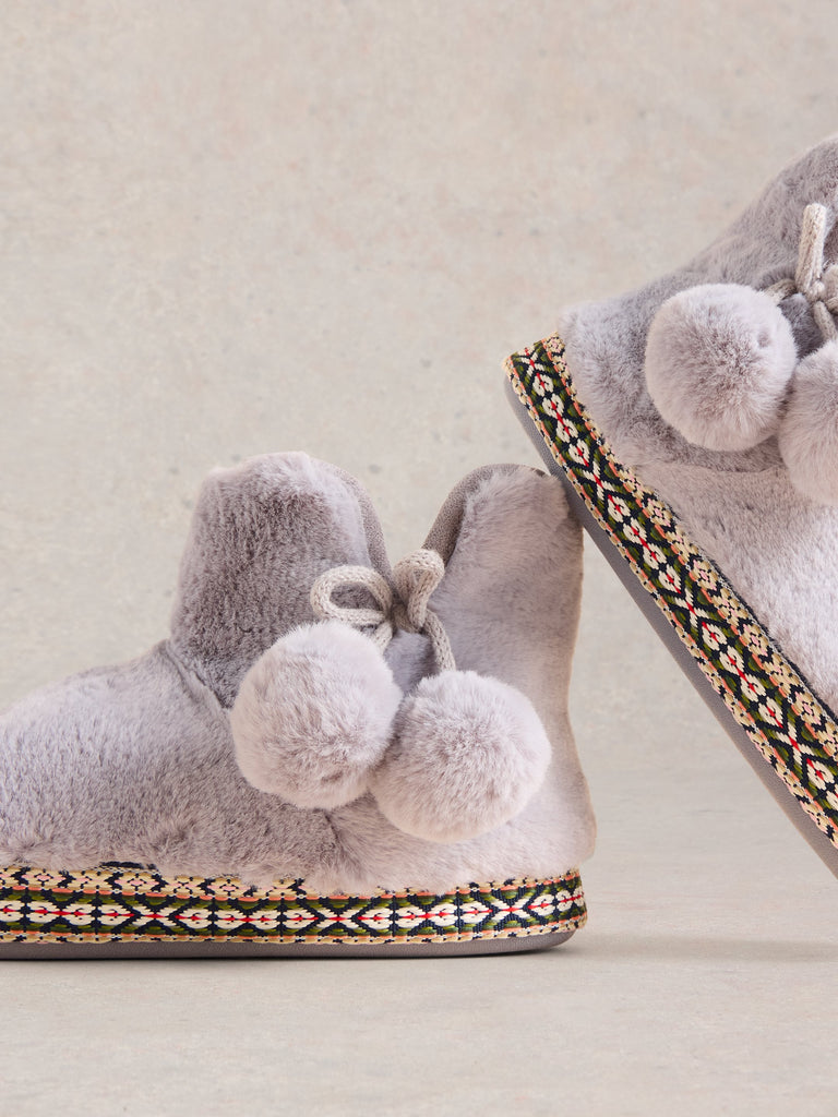 Pair of gray faux fur slippers with pom-poms and patterned trim.