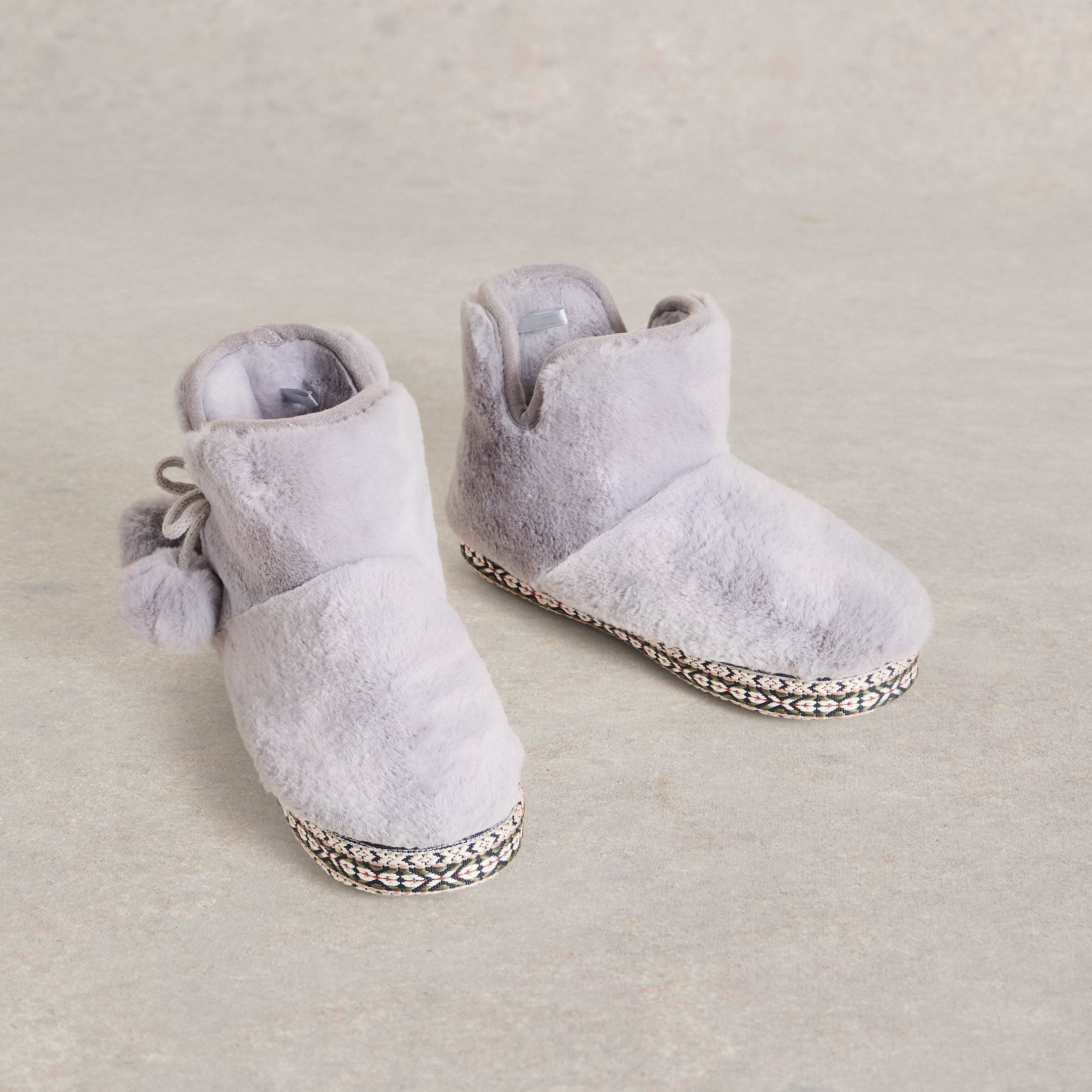 Pair of gray faux fur slipper boots with pom-pom detail and patterned trim.