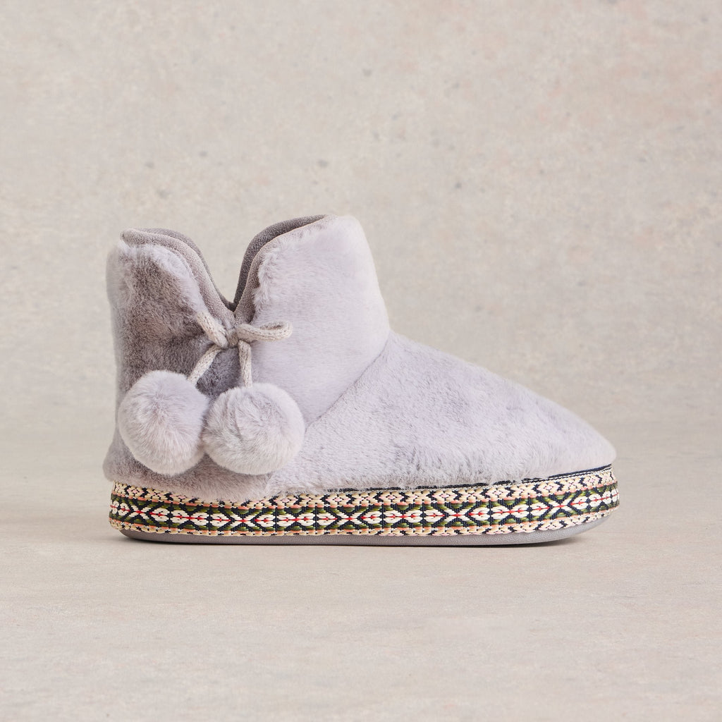 Grey fuzzy slipper boot with pom-pom accents and patterned trim.