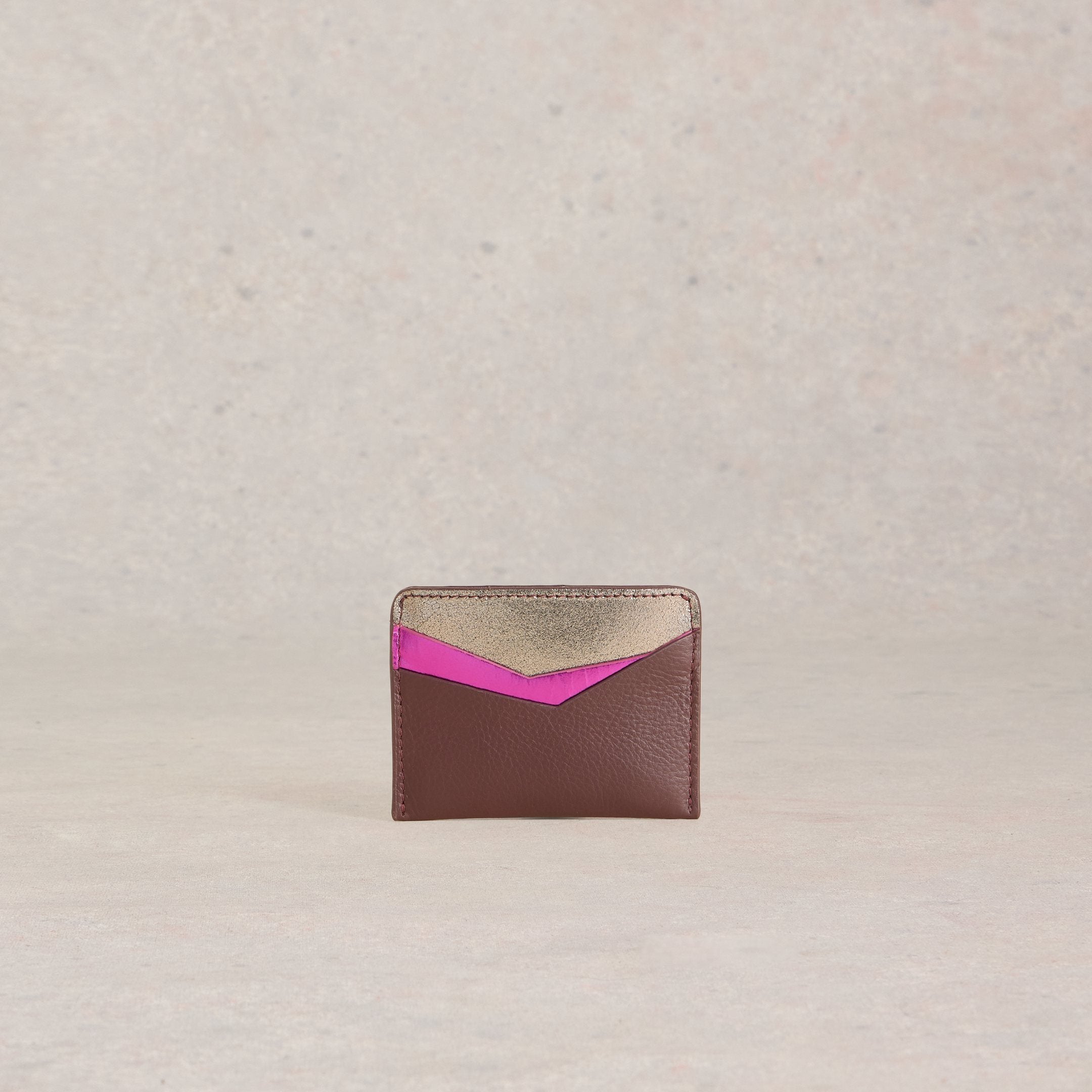 Brown leather cardholder with gold and fuchsia accents. The fuchsia forms a V-shape against the gold.