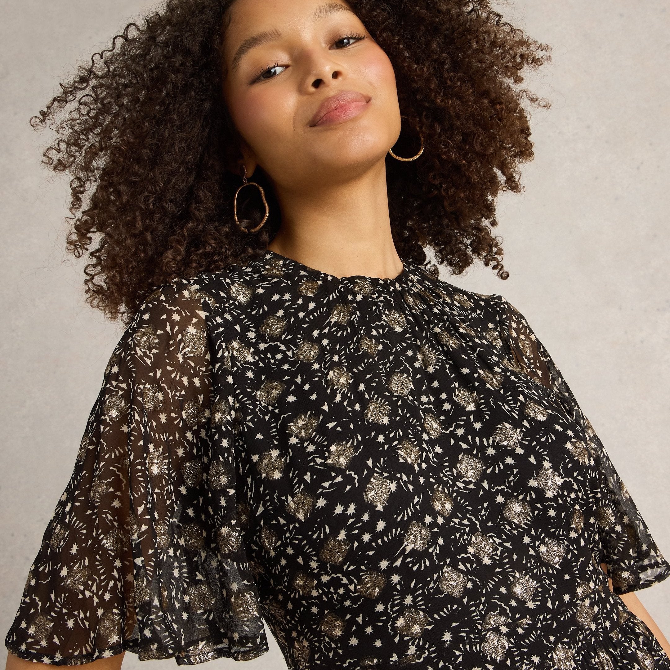 Black mini dress with gold star print and flutter sleeves.