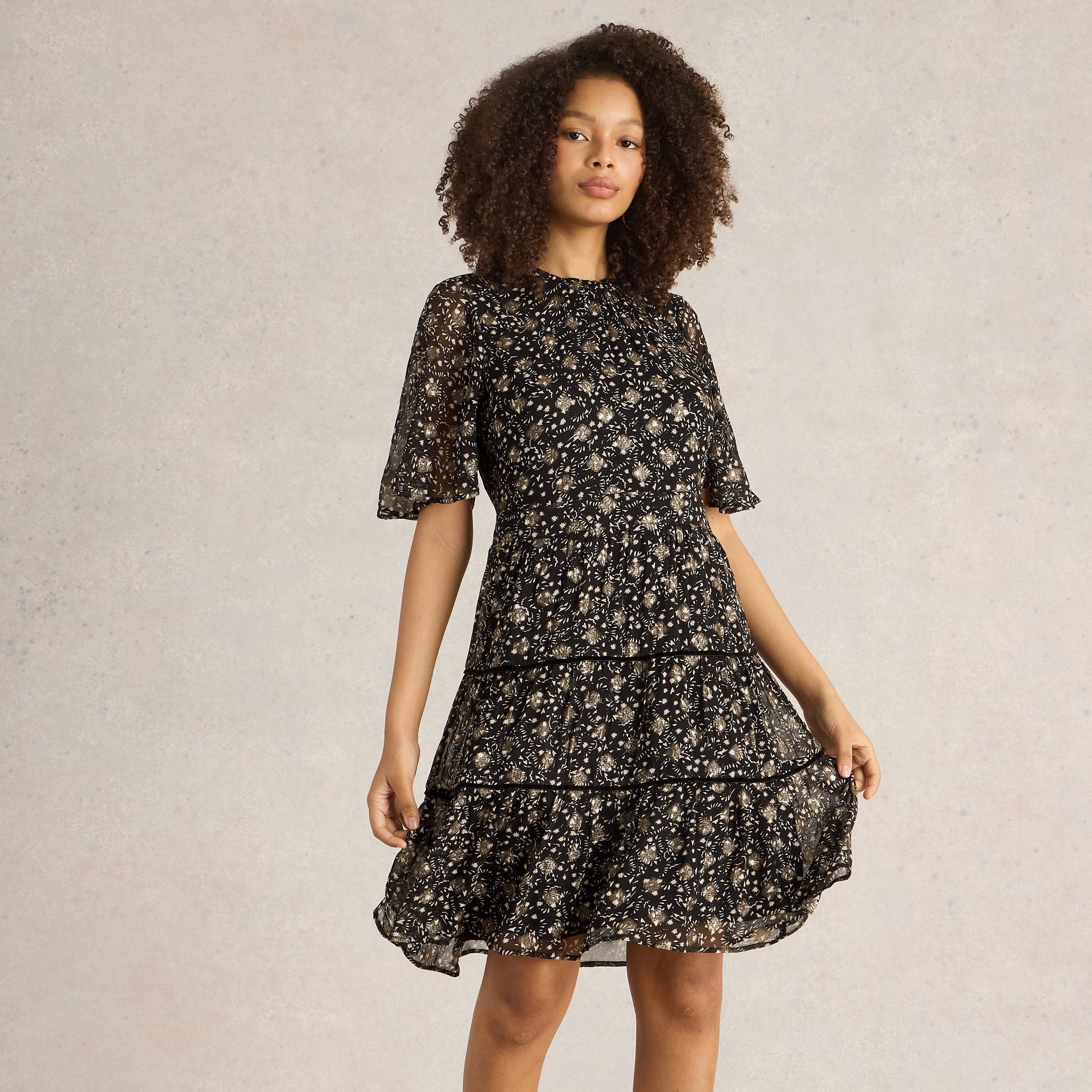 Black tiered mini dress with gold floral print and short sleeves.