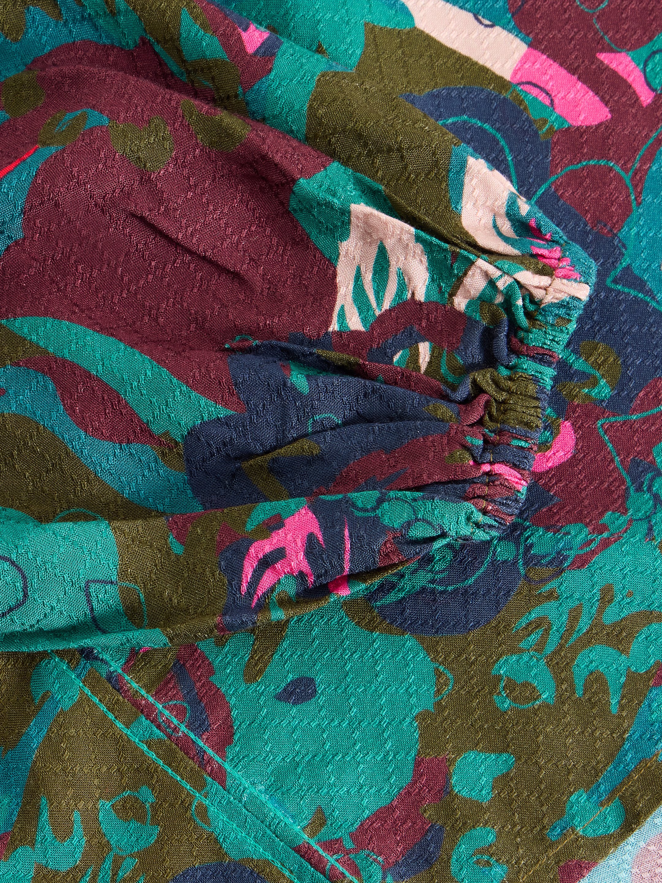 Close-up of textured fabric with an abstract floral print in teal, burgundy, olive green, and pink.