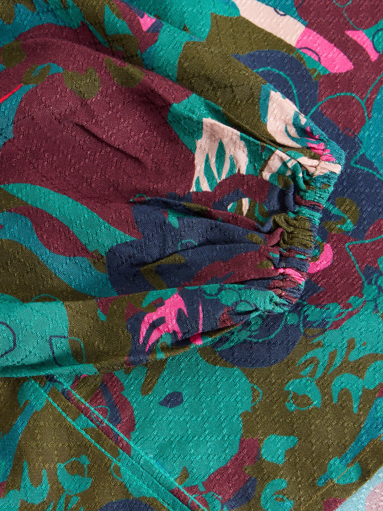Close-up of textured fabric with an abstract floral print in teal, burgundy, olive green, and pink.