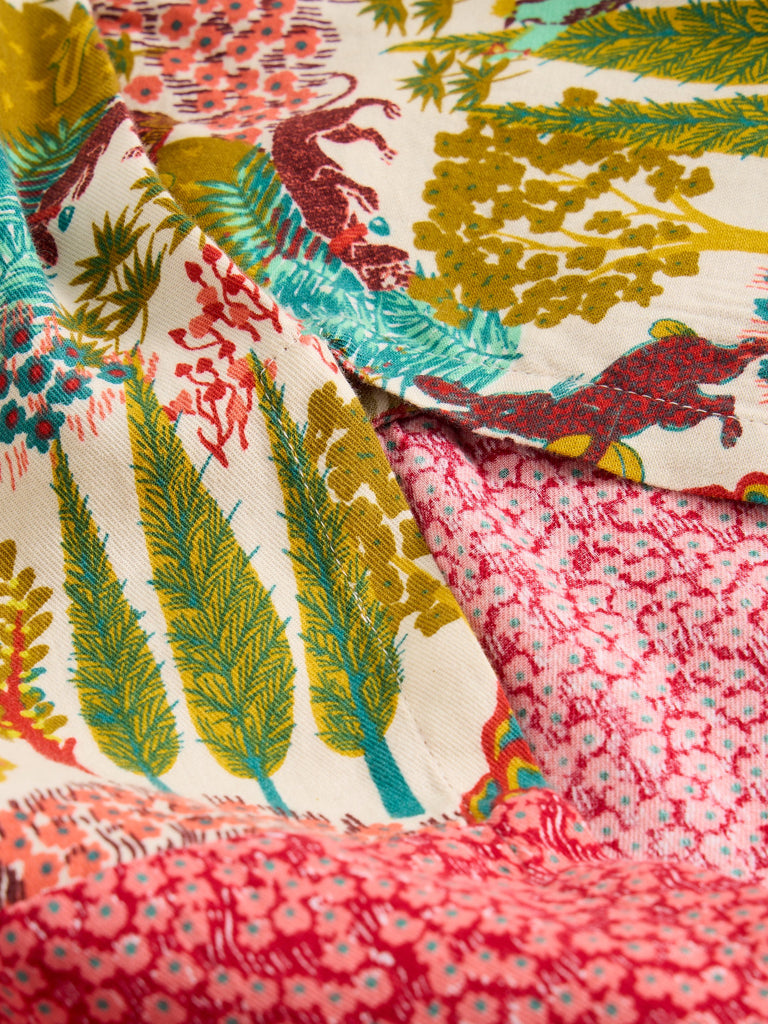 Close-up of cream fabric with a multicolored print featuring stylized animals, trees, and floral designs.