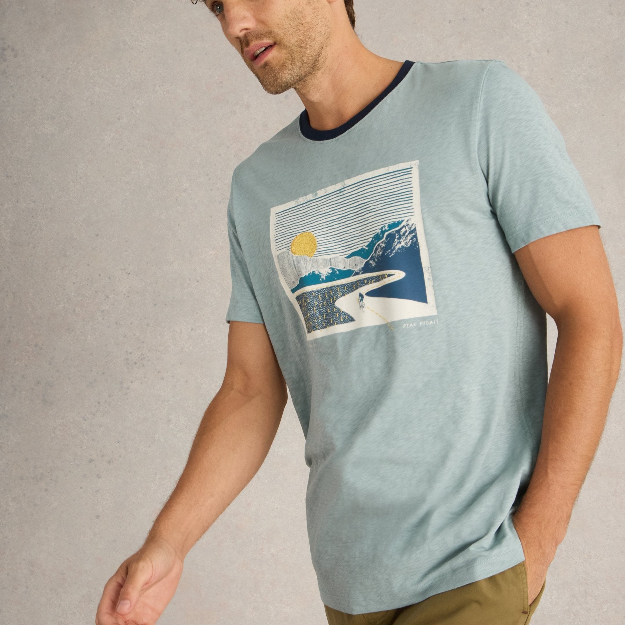 Light blue short-sleeve t-shirt featuring a graphic print of a cyclist riding through a mountain landscape at sunset.