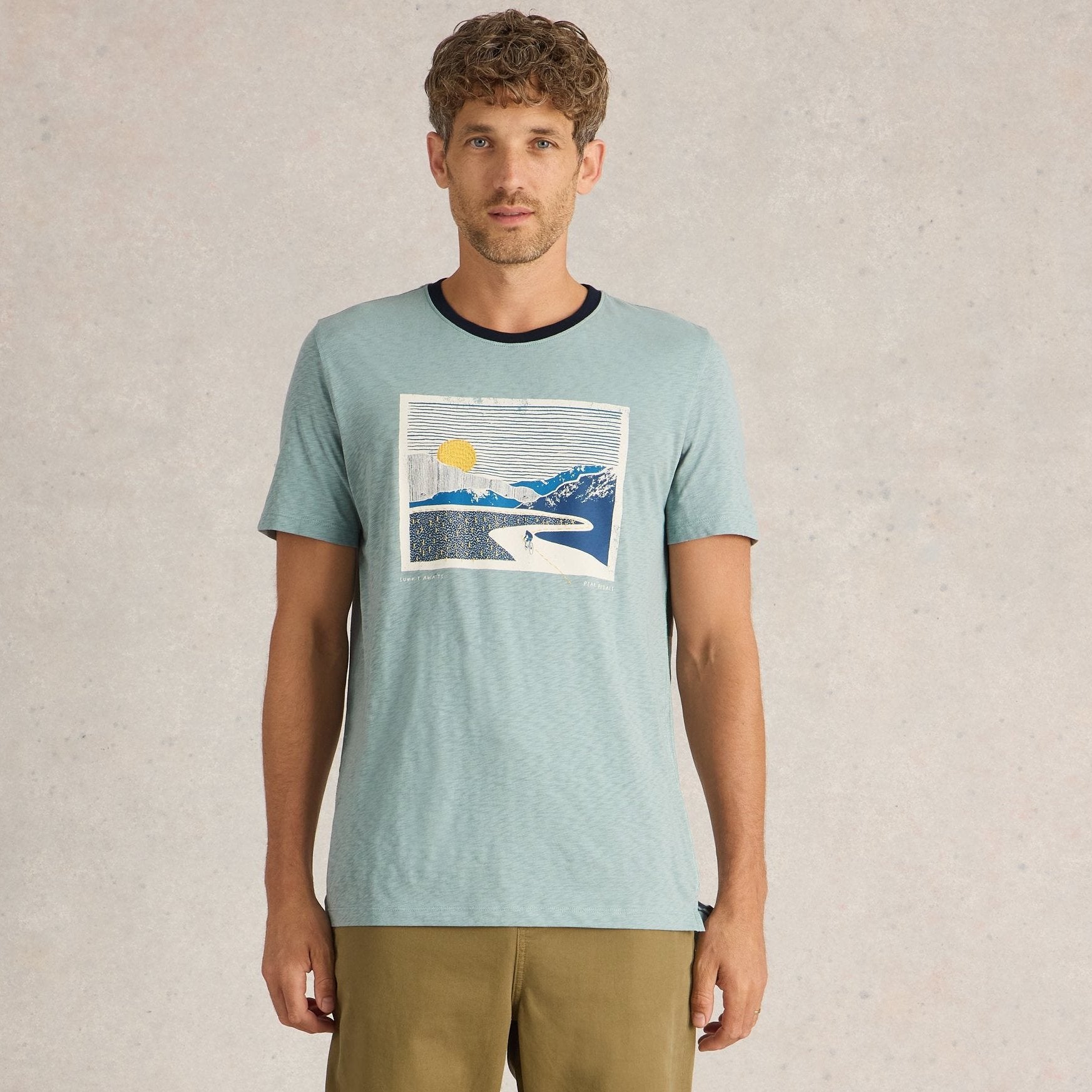 Light teal short-sleeved t-shirt featuring a rectangular graphic print of a cyclist on a winding road, set against a