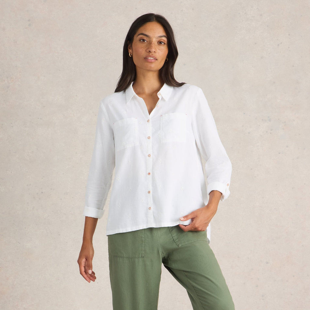 Woman wearing a white shirt and green pants against a beige background