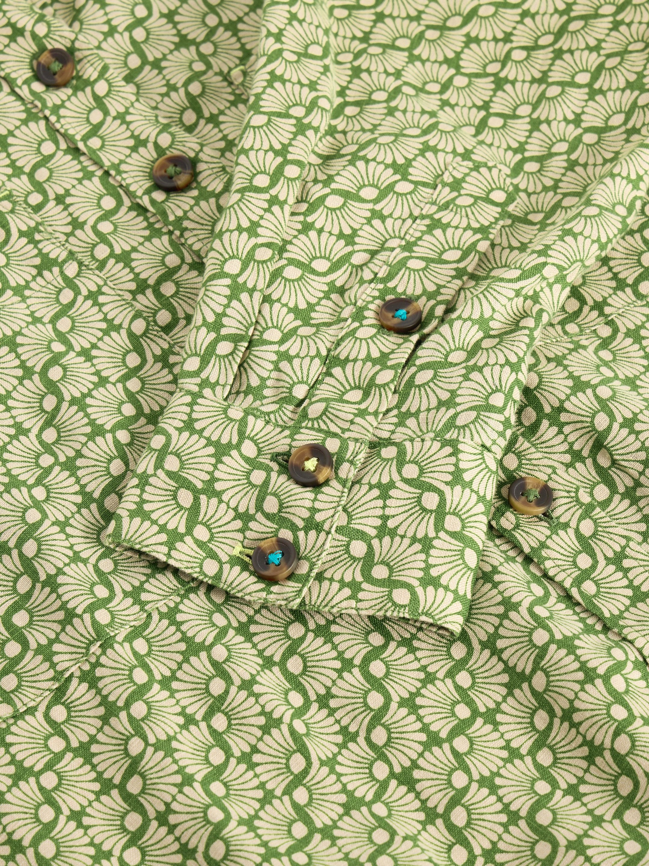Close-up of a green and cream patterned shirt with tortoiseshell buttons. The fabric features a repeating floral design.