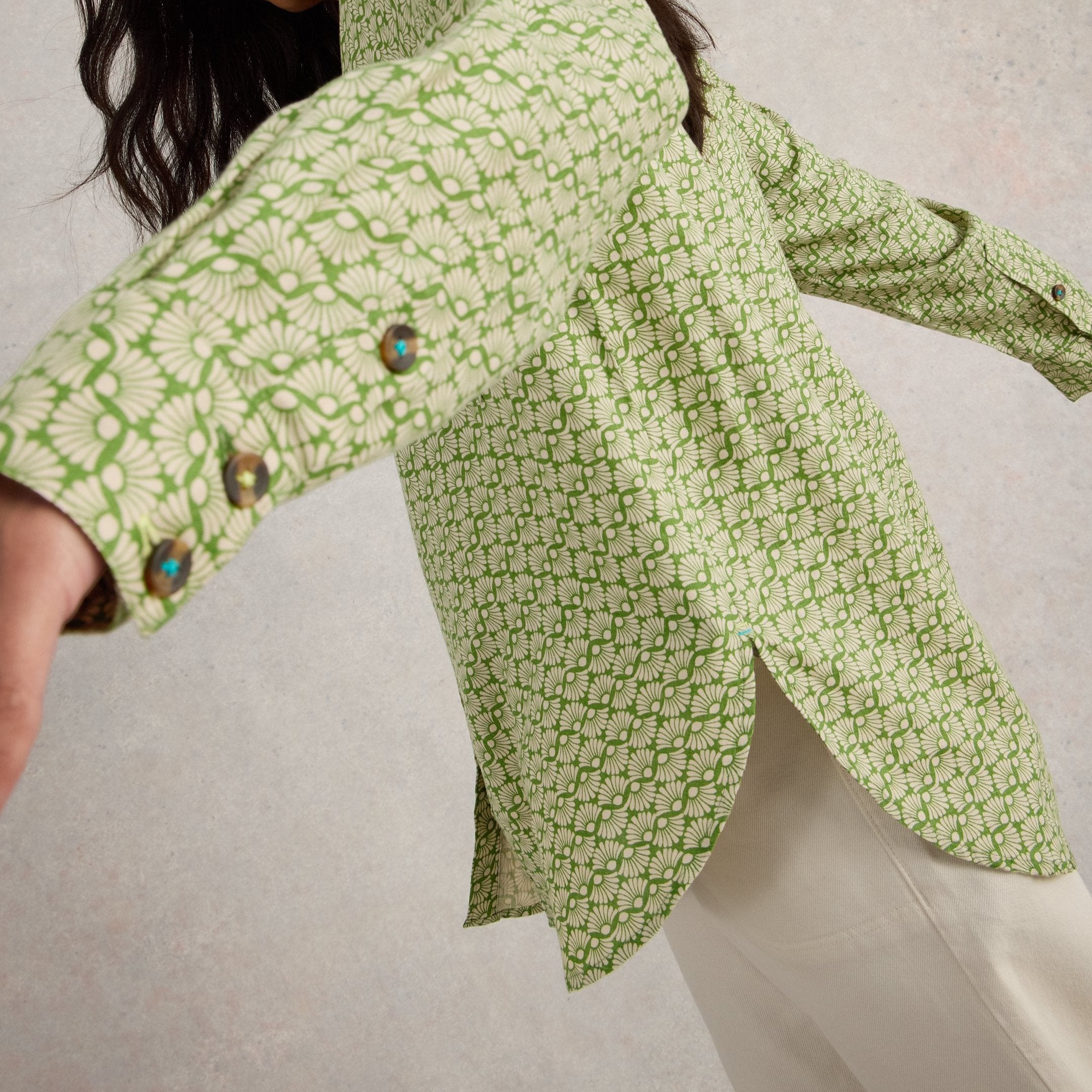 Long-sleeved green shirt with a repeating off-white floral pattern and decorative buttons.