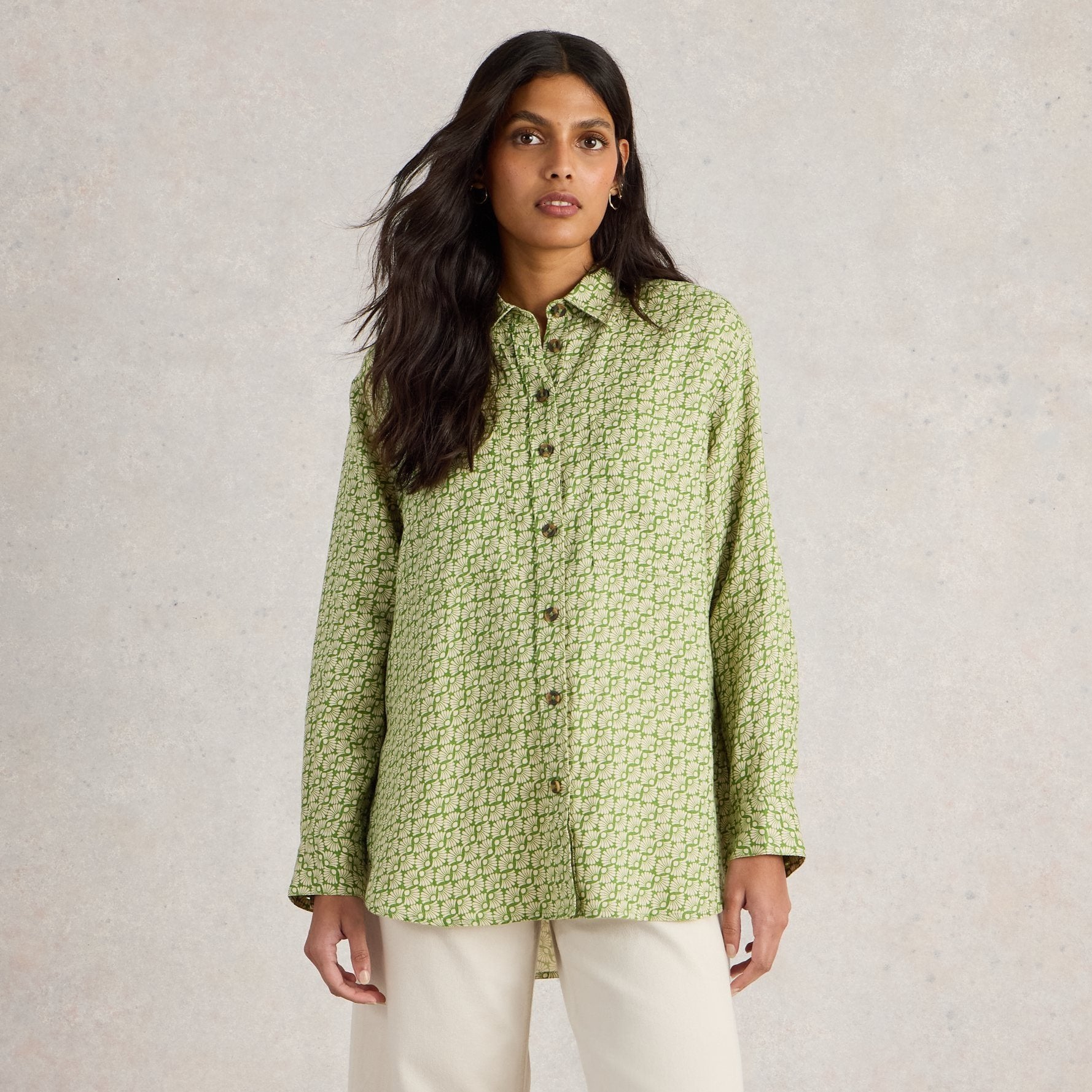 Green, long-sleeved button-down shirt with a repeating floral pattern. The shirt has a relaxed fit and falls to the hip.