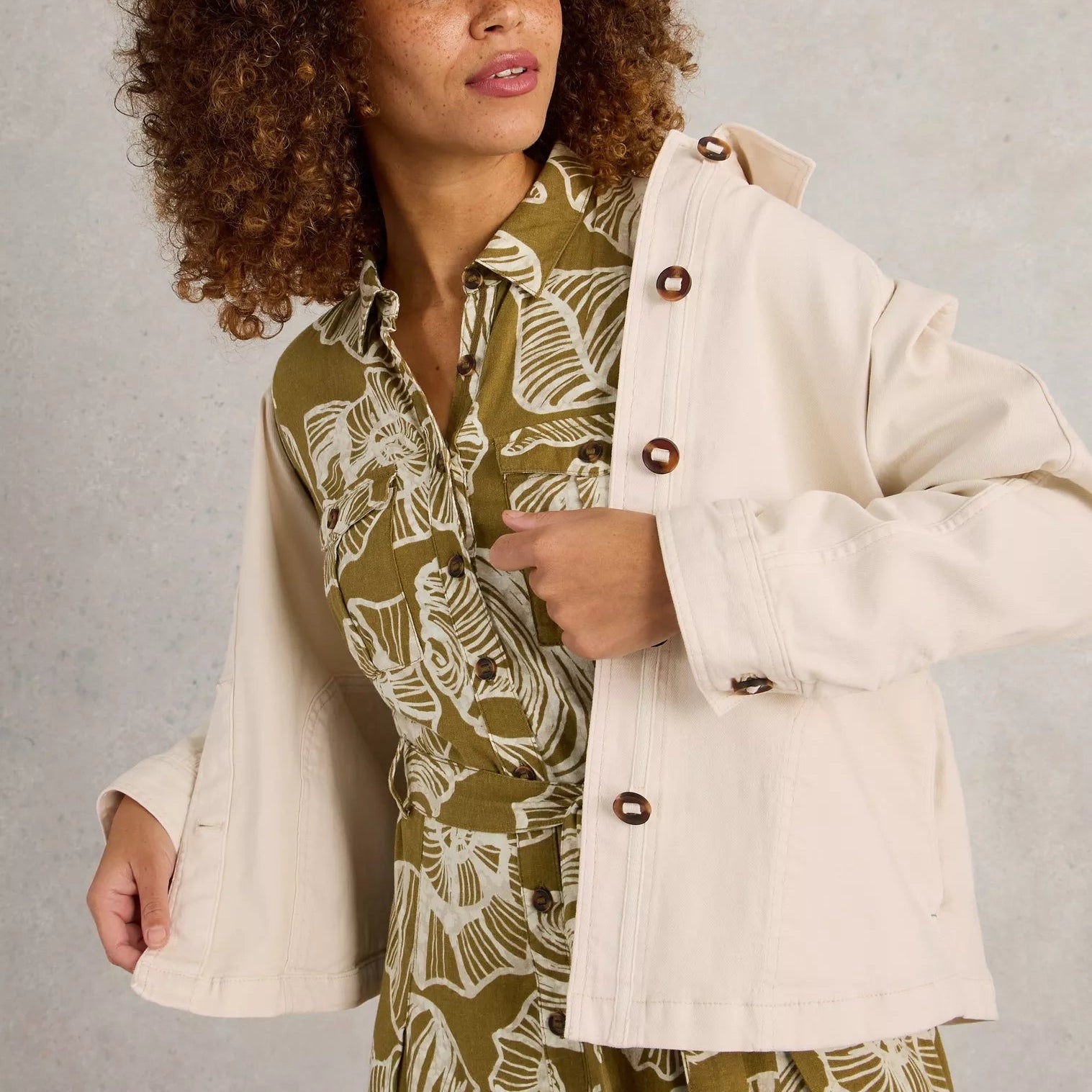 Woman wearing a white jacket over a green patterned outfit on a neutral background