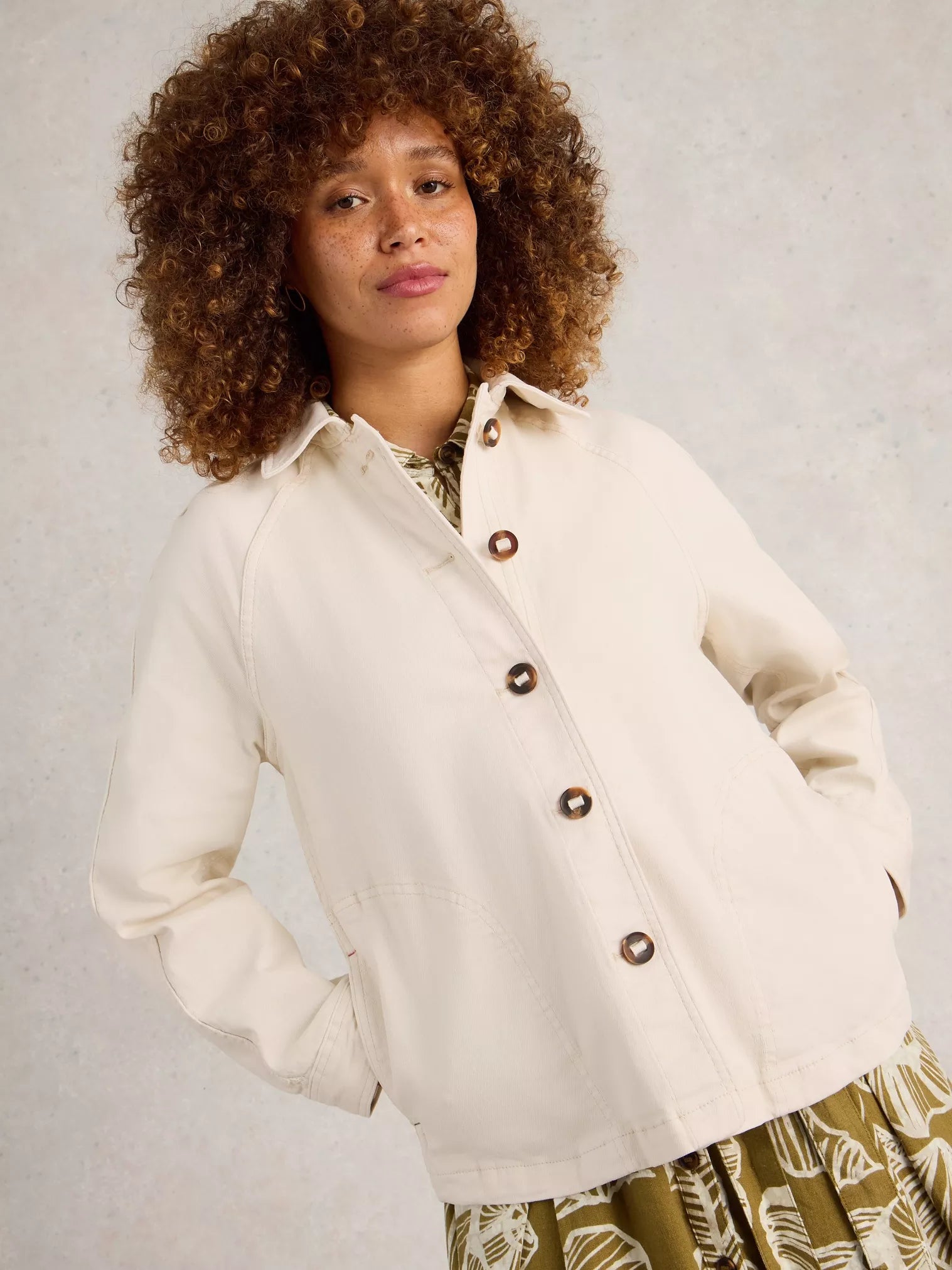 Woman wearing a white jacket with brown buttons against a plain background