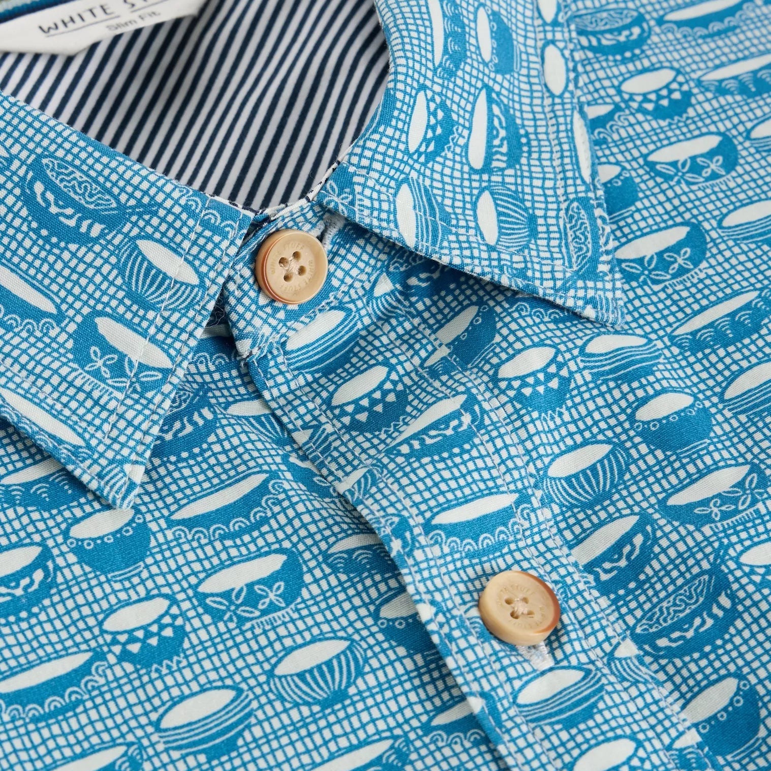 Close-up of a teal shirt with a white grid pattern and a repeating design of stylized bowls.