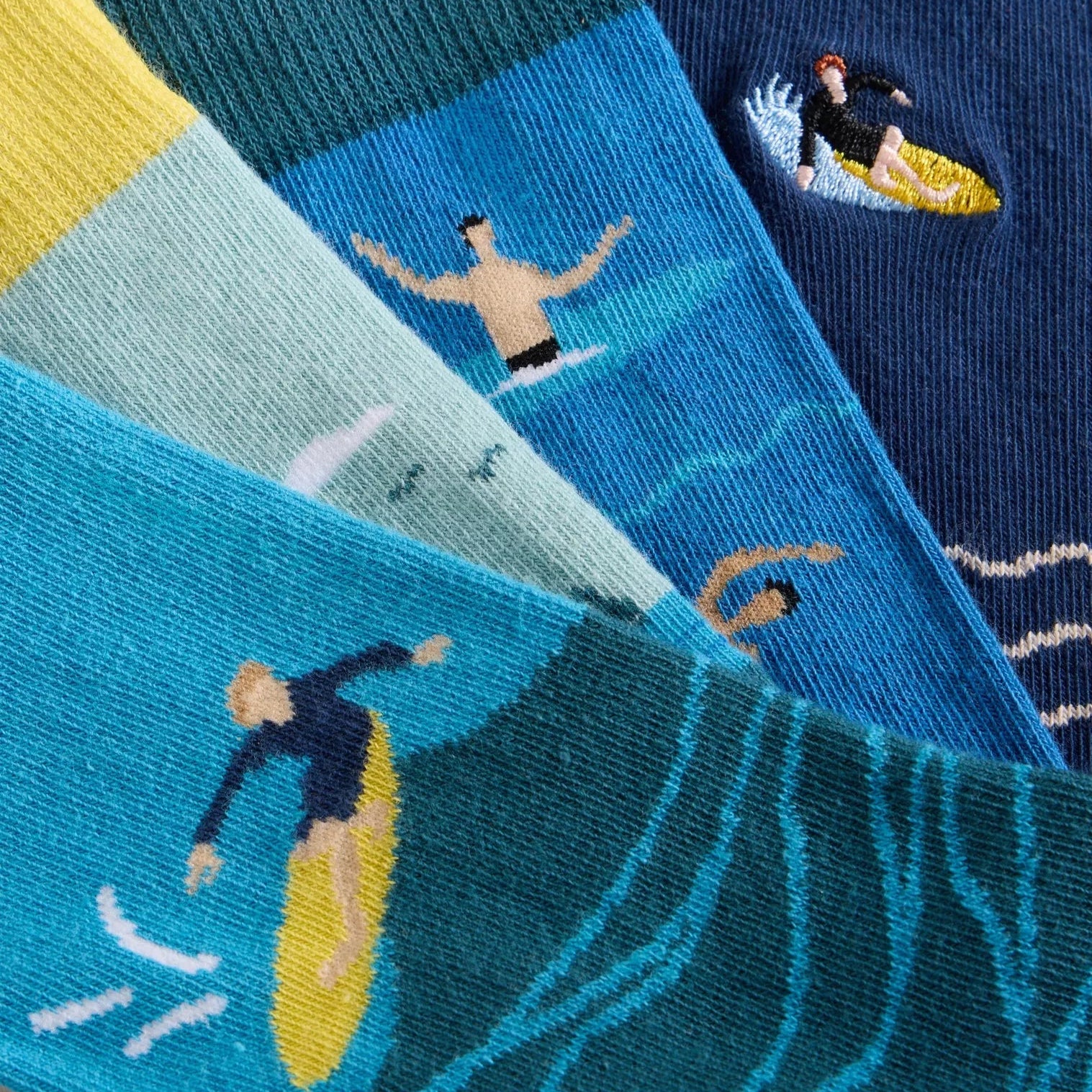 Close-up of a stack of socks featuring surfers and ocean waves in various shades of blue and teal.