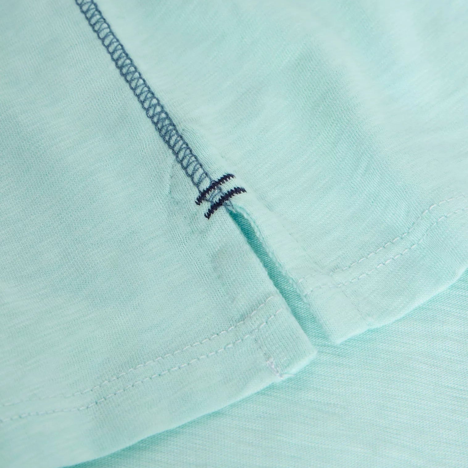 Close-up of light teal fabric with a center back seam featuring a small, reinforced opening. The stitching is visible.