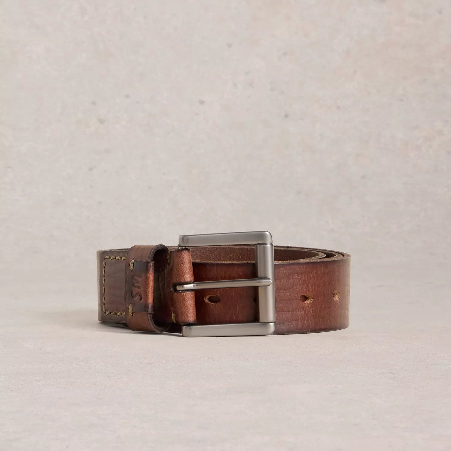 Brown leather belt with silver buckle on a beige background