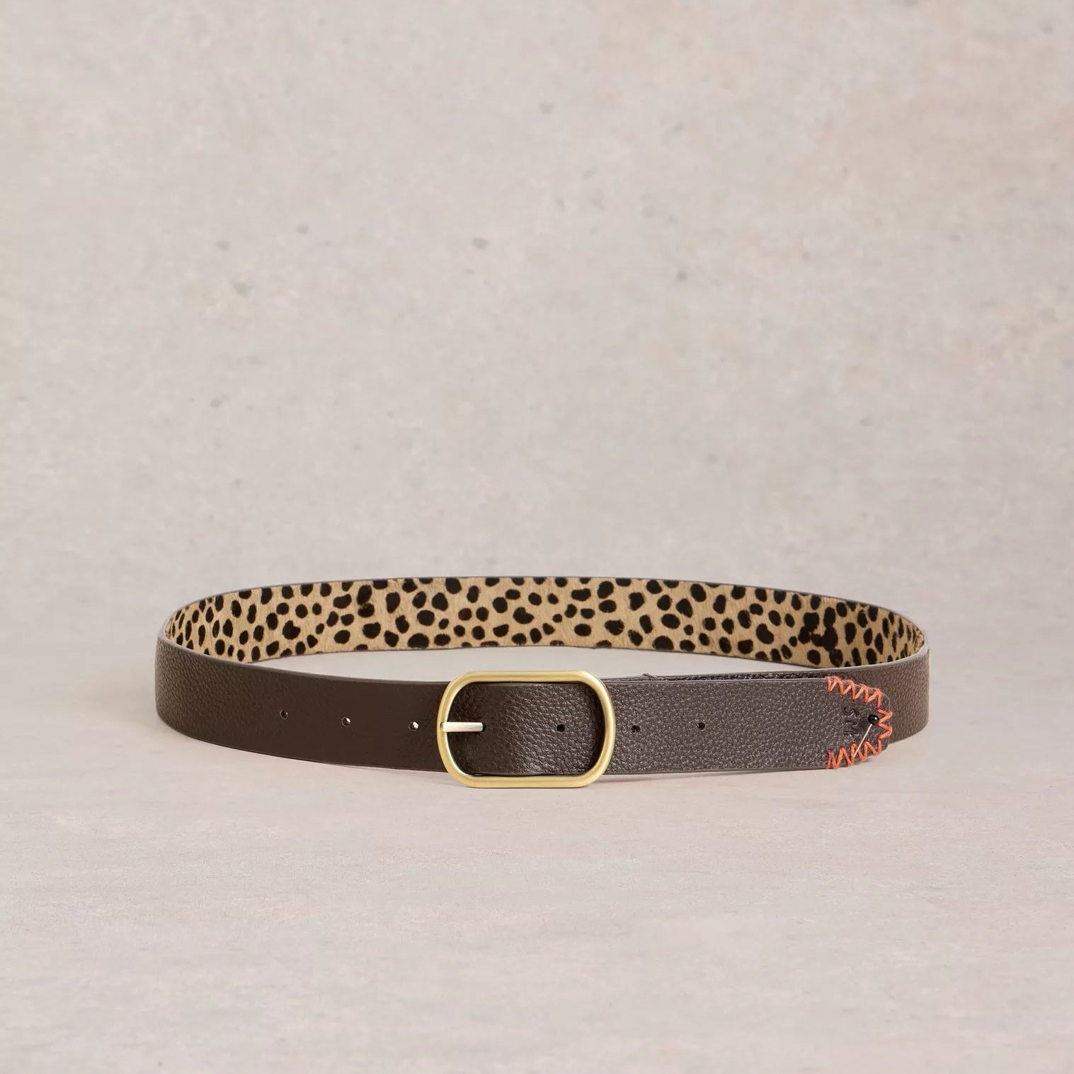 Brown leather belt with a gold buckle and leopard print lining. Orange stitching detail is visible on one end.