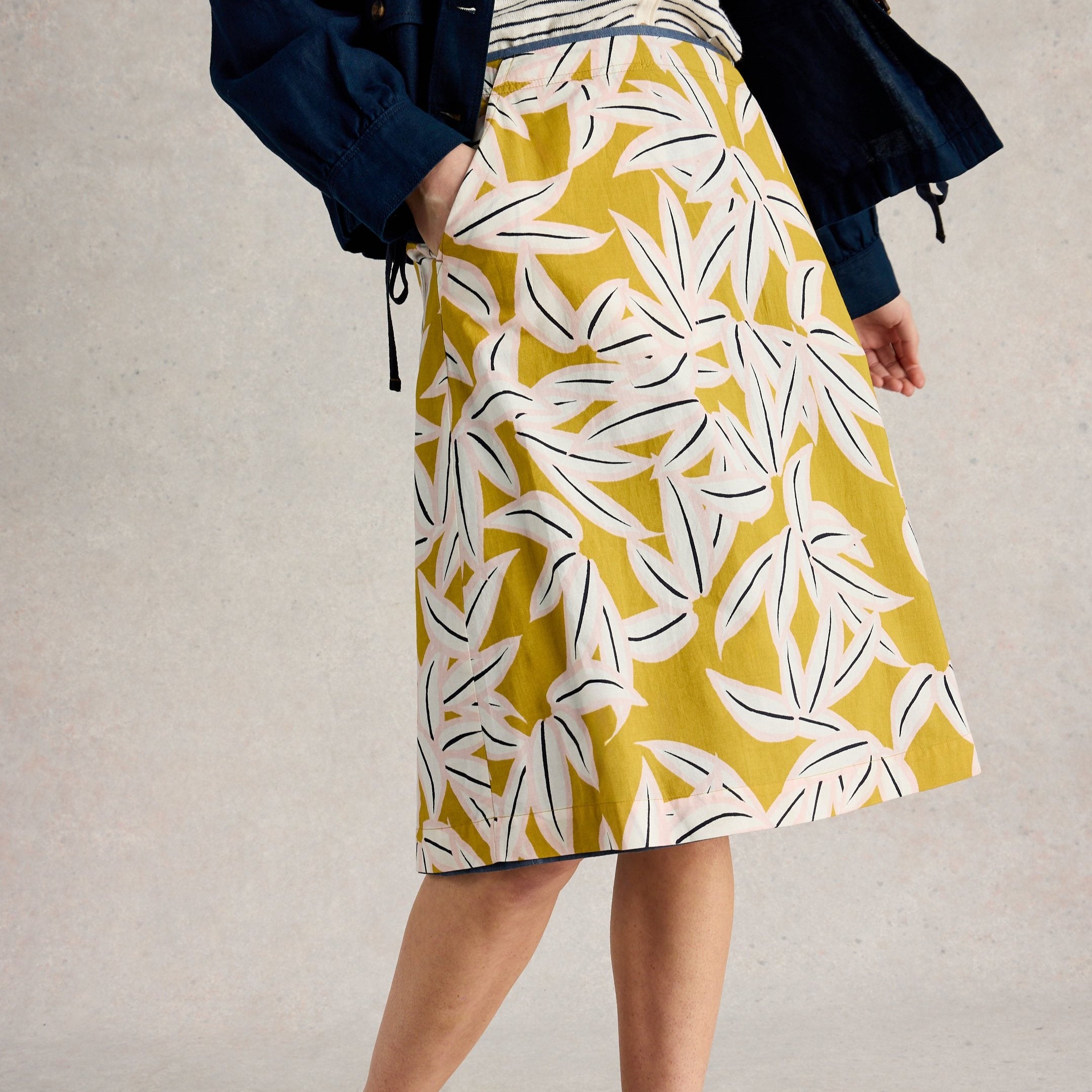 Mustard yellow midi skirt with a stylized leaf print in pink and black. The skirt has pockets and a slightly A-line shape.