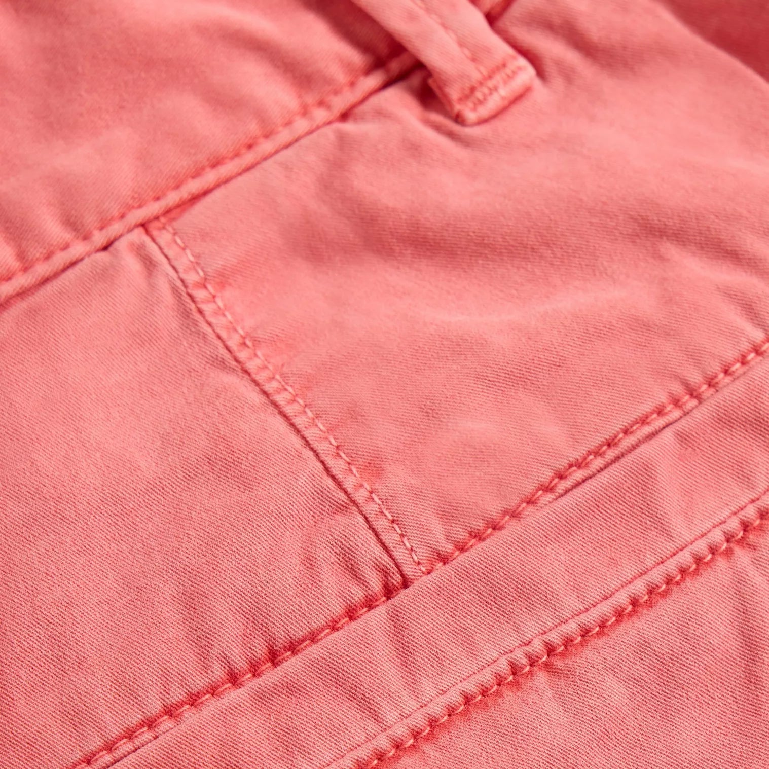 Close-up of coral-colored twill fabric with visible stitching detail.
