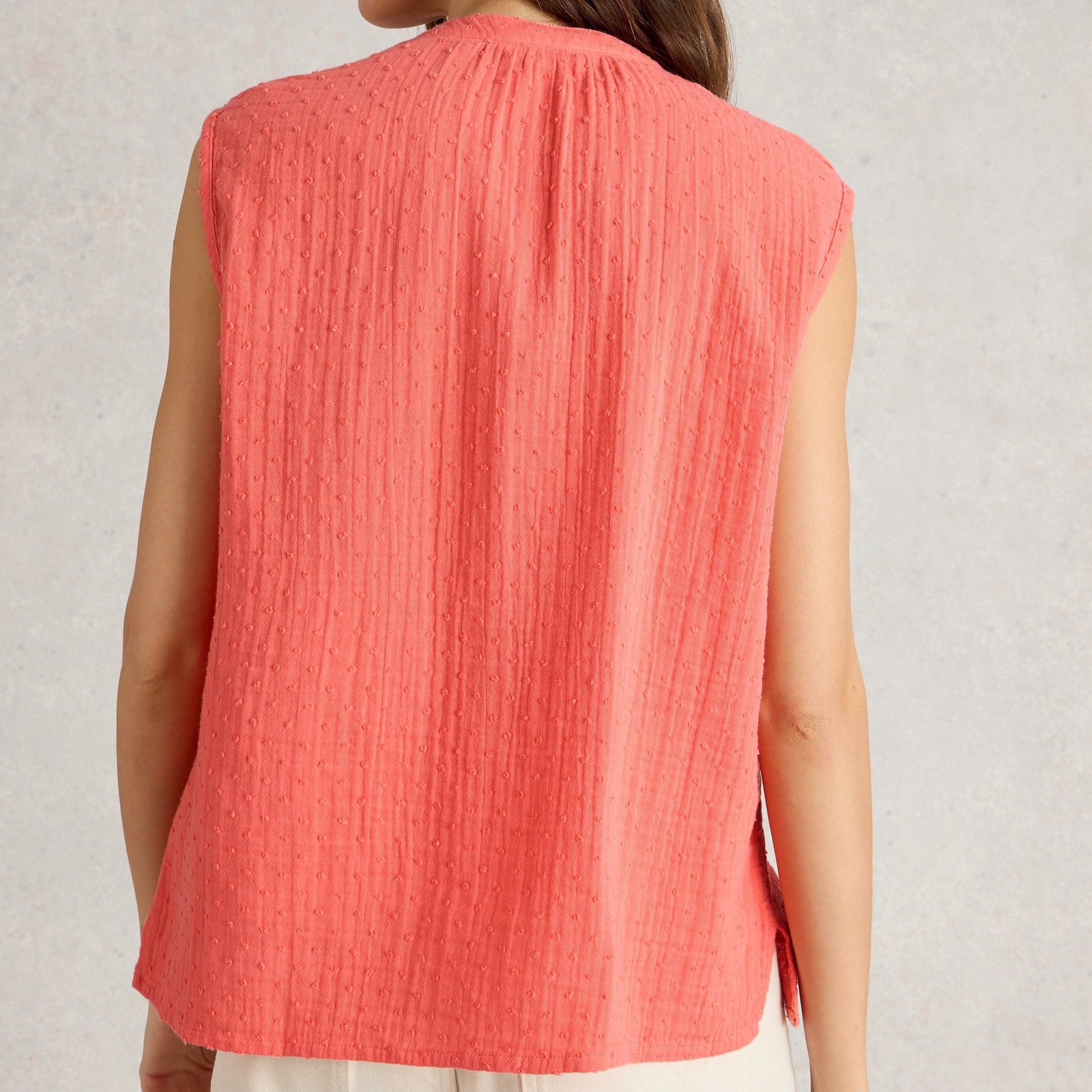Coral sleeveless top with textured fabric and a slightly rounded neckline.