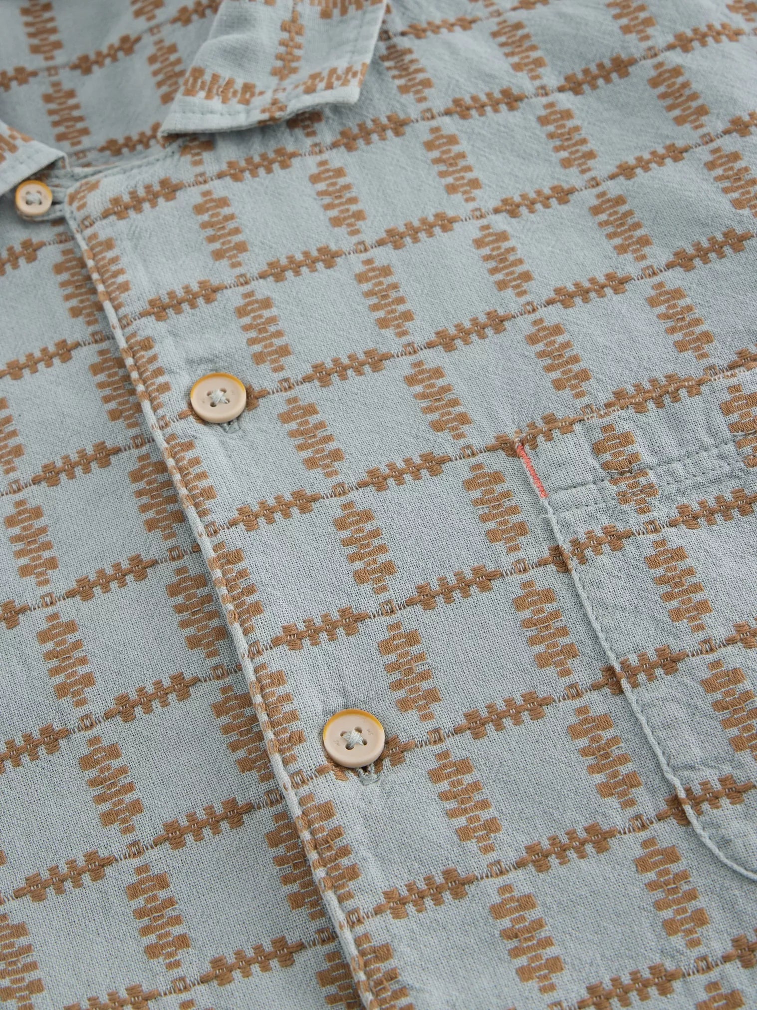 Close-up of a light blue woven shirt with a brown grid pattern, featuring button closures and a chest pocket.