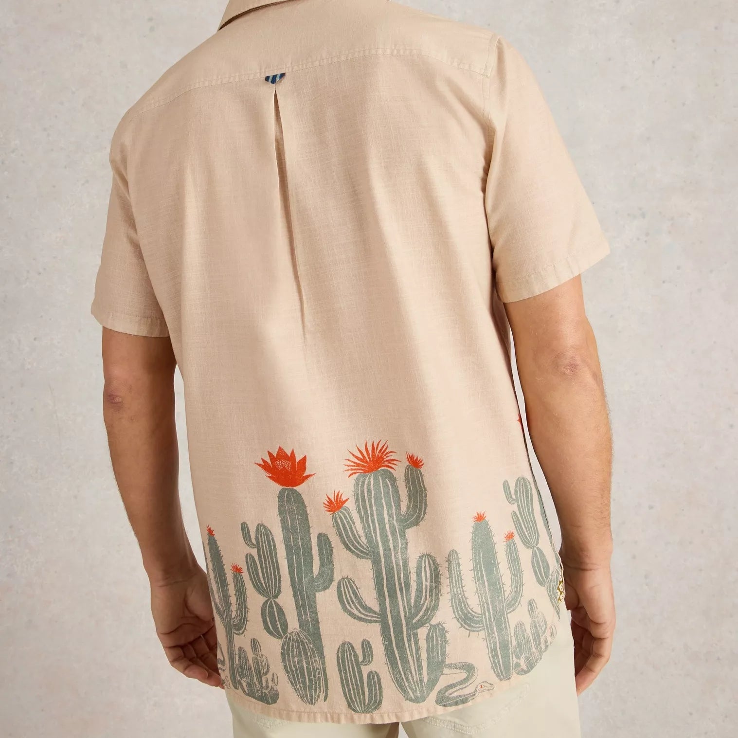 Beige linen short-sleeve shirt with a bottom hem featuring a repeating pattern of cacti and a snake.