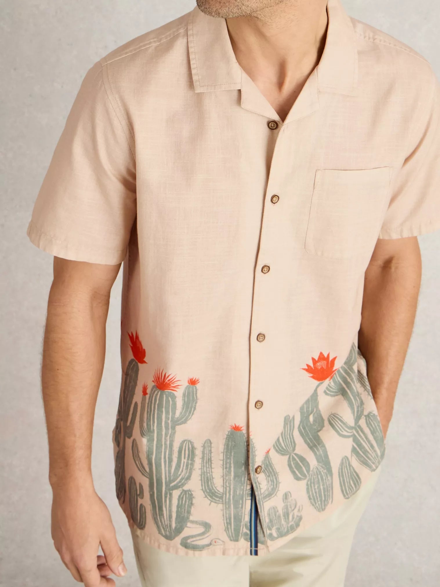 Beige linen short-sleeve shirt with a cactus and floral print at the bottom hem.