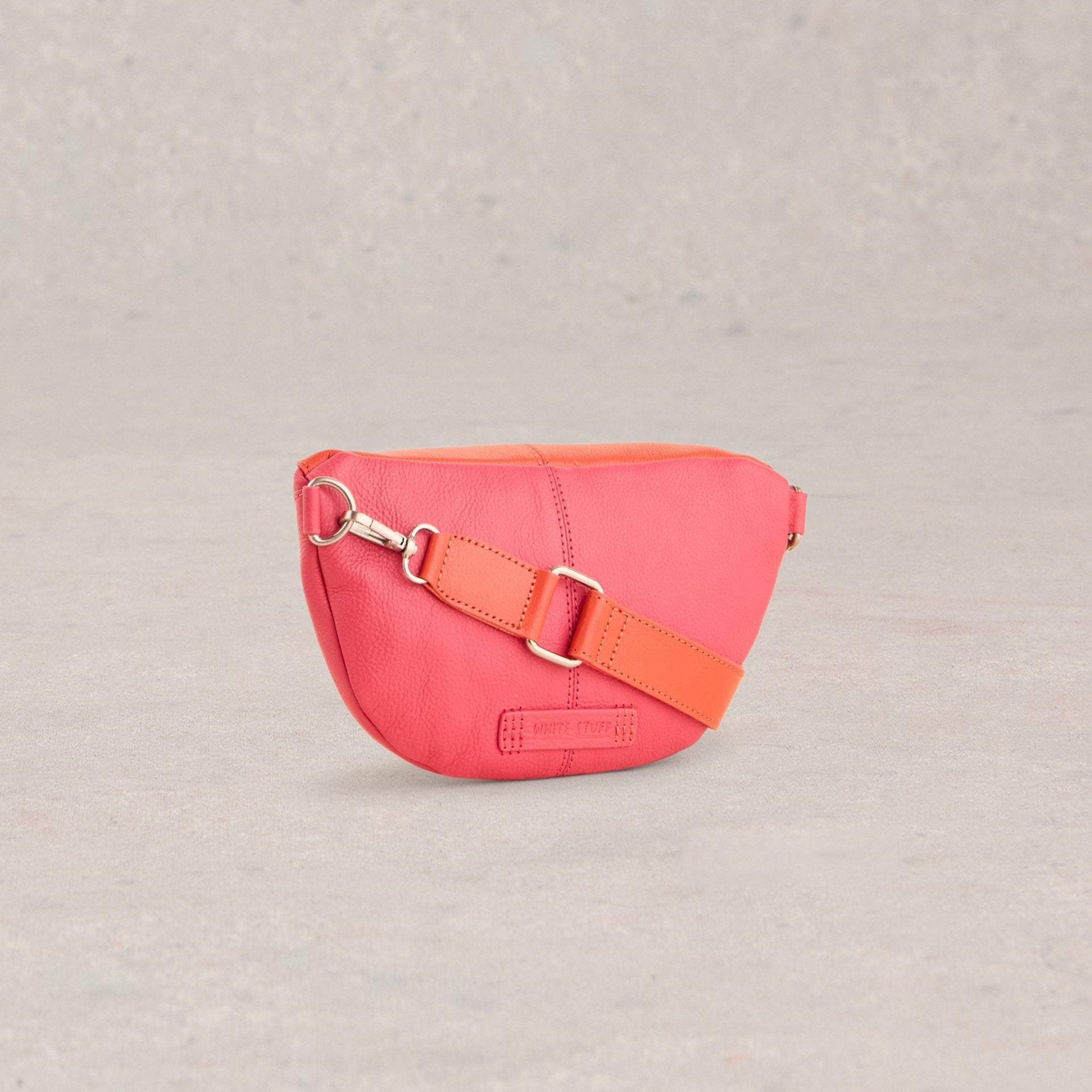 Pink leather crossbody bag with an orange strap. The bag is curved and has a small silver clasp.