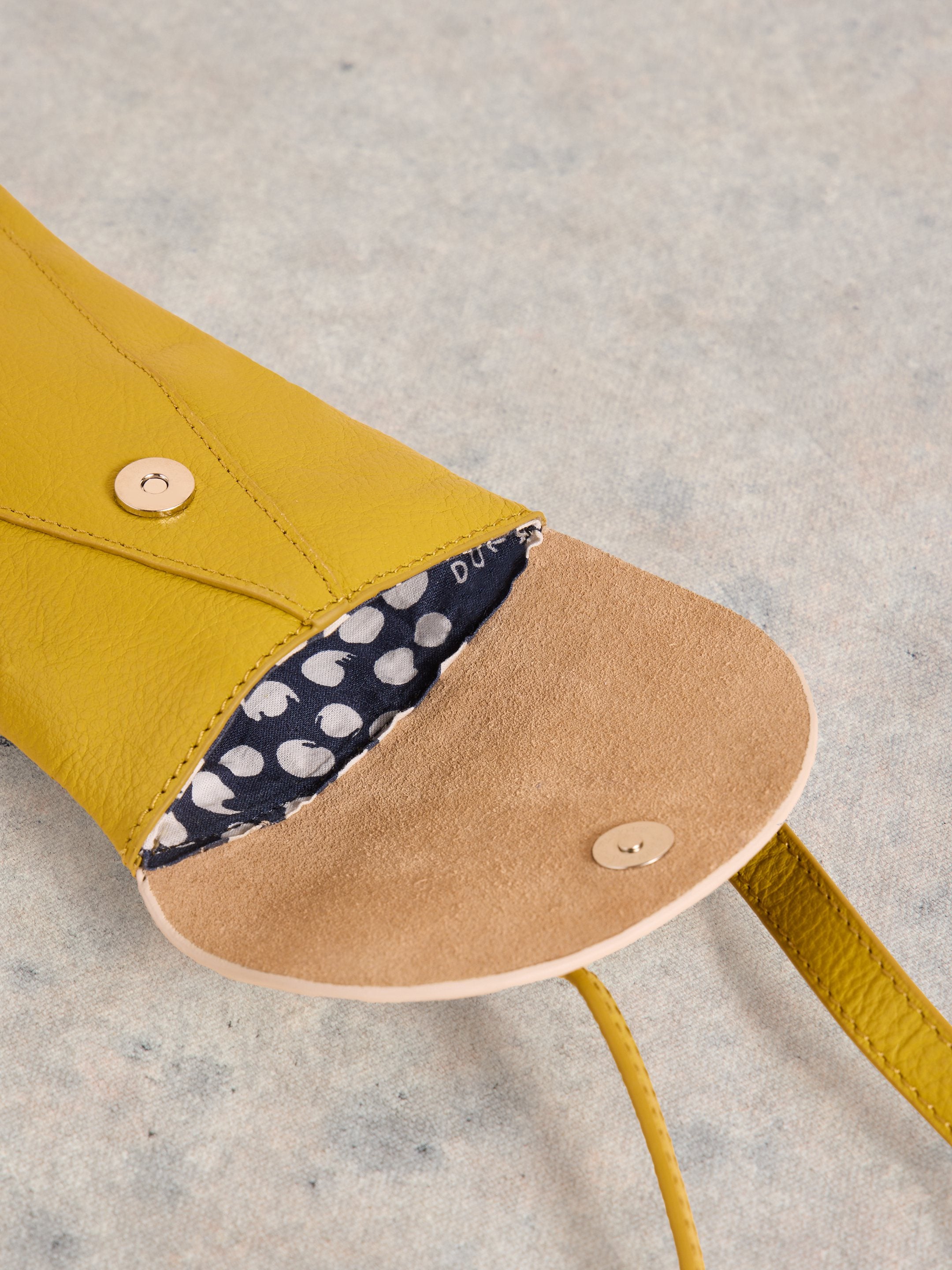 Mustard yellow leather crossbody bag with tan suede interior and navy polka dot fabric lining. Gold-toned magnetic closures.