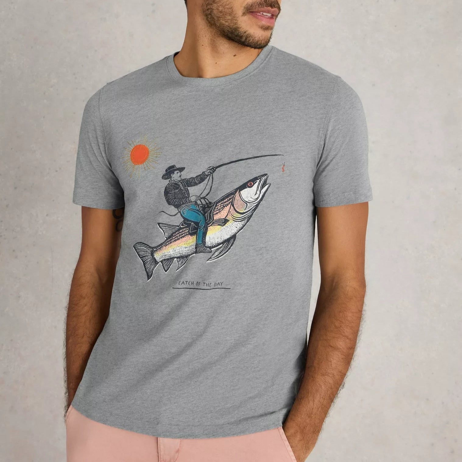 Gray short-sleeve t-shirt featuring a graphic print of a man fishing from atop a large fish; text below reads "Catch of the