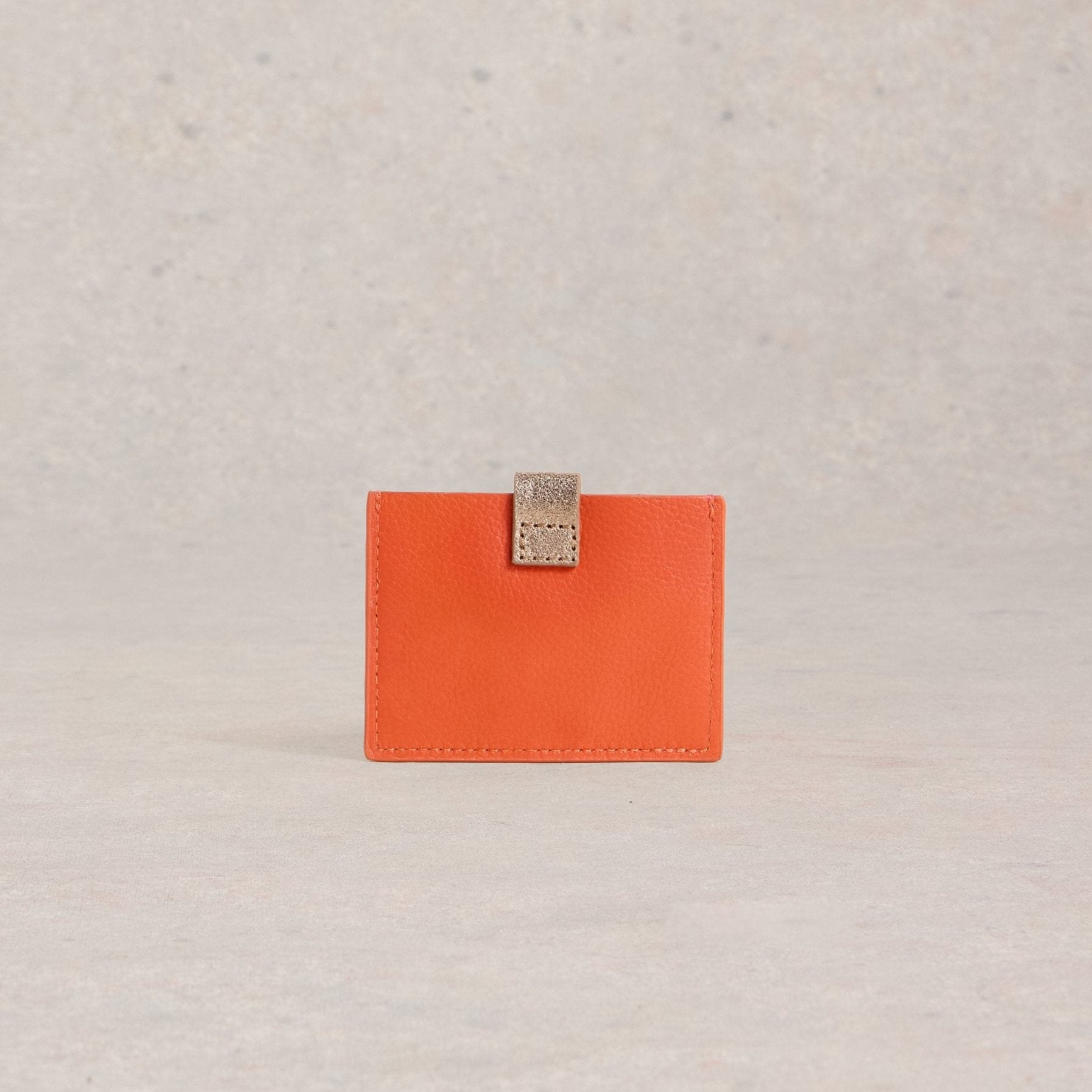 Orange leather cardholder with a light gold closure tab.