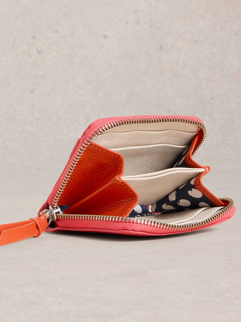 Coral pink leather zip-around wallet open to reveal multiple card slots and a patterned interior.