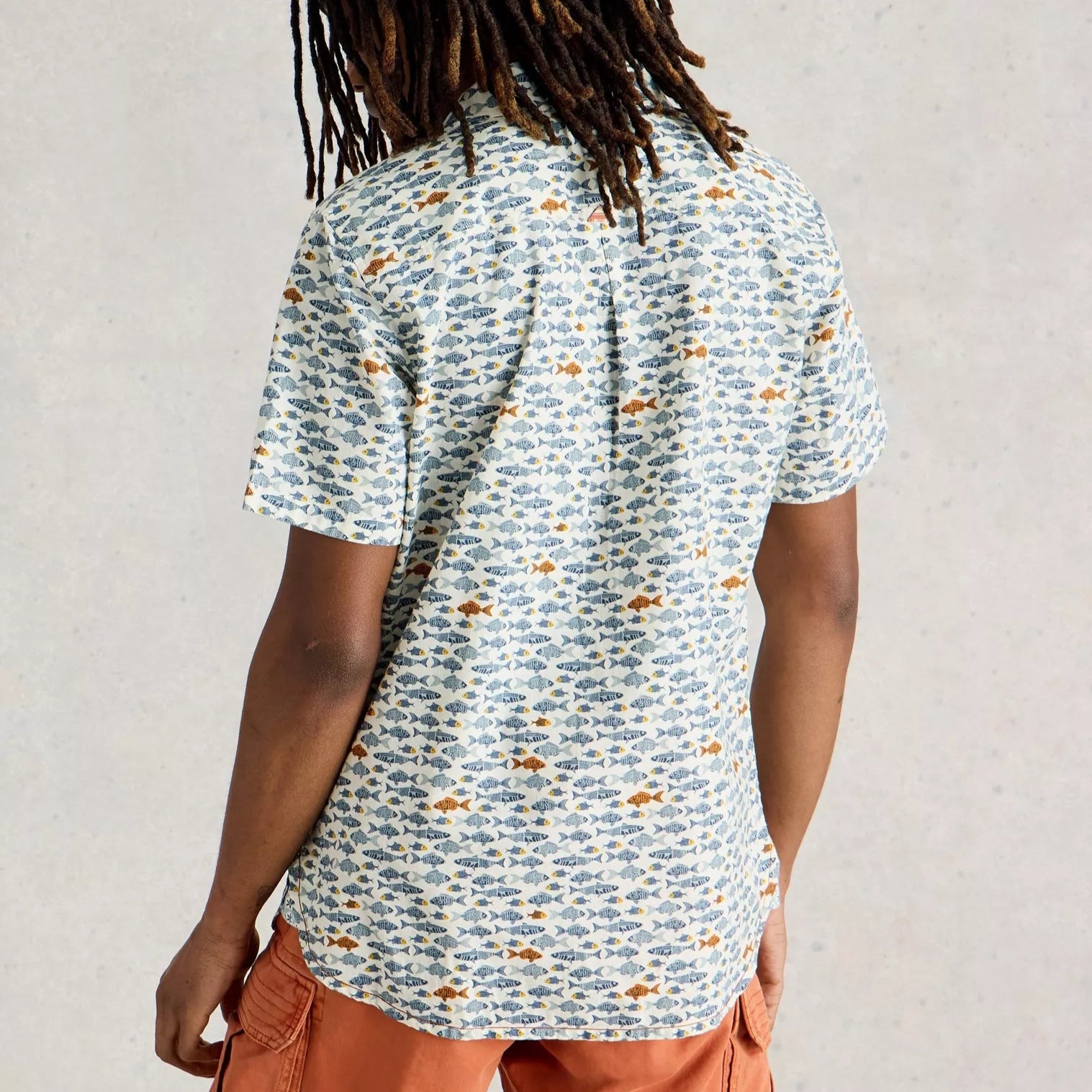 Short-sleeved button-down shirt with an all-over print of small, stylized fish in blue and orange on a cream background.