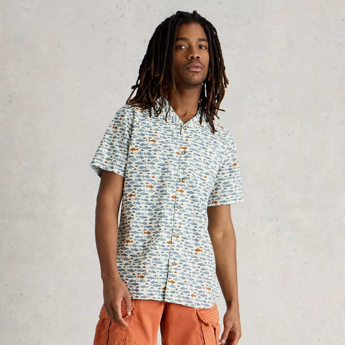 Men's short-sleeve button-down shirt with an all-over print of small, stylized fish in blue, orange, and gray on a cream