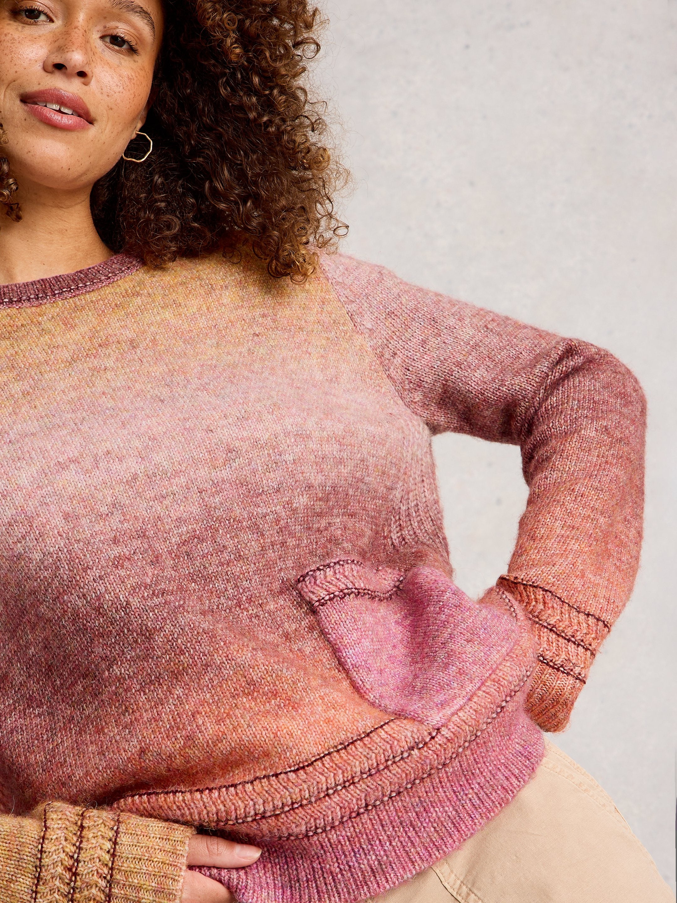 Woman wearing a pink and brown gradient sweater against a plain background