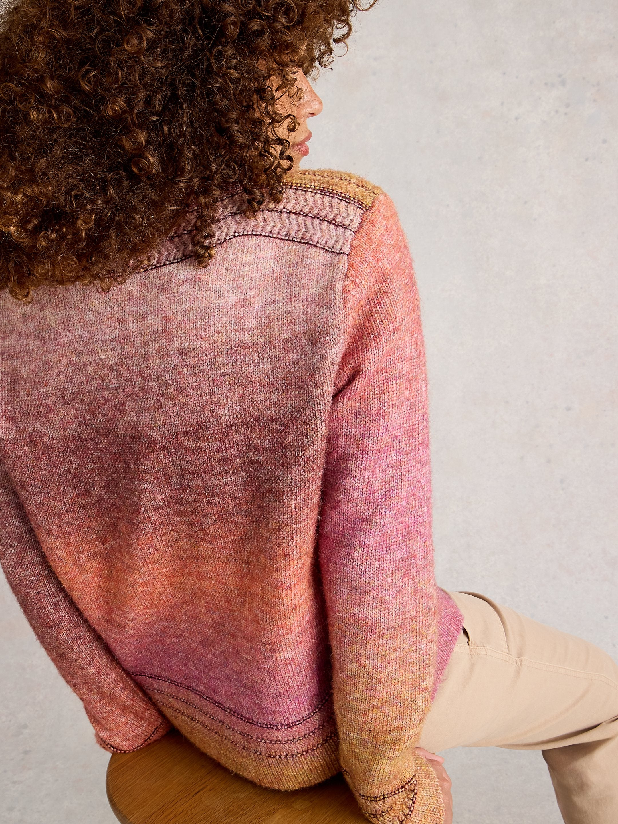Person wearing a gradient sweater sitting on a wooden stool against a plain background