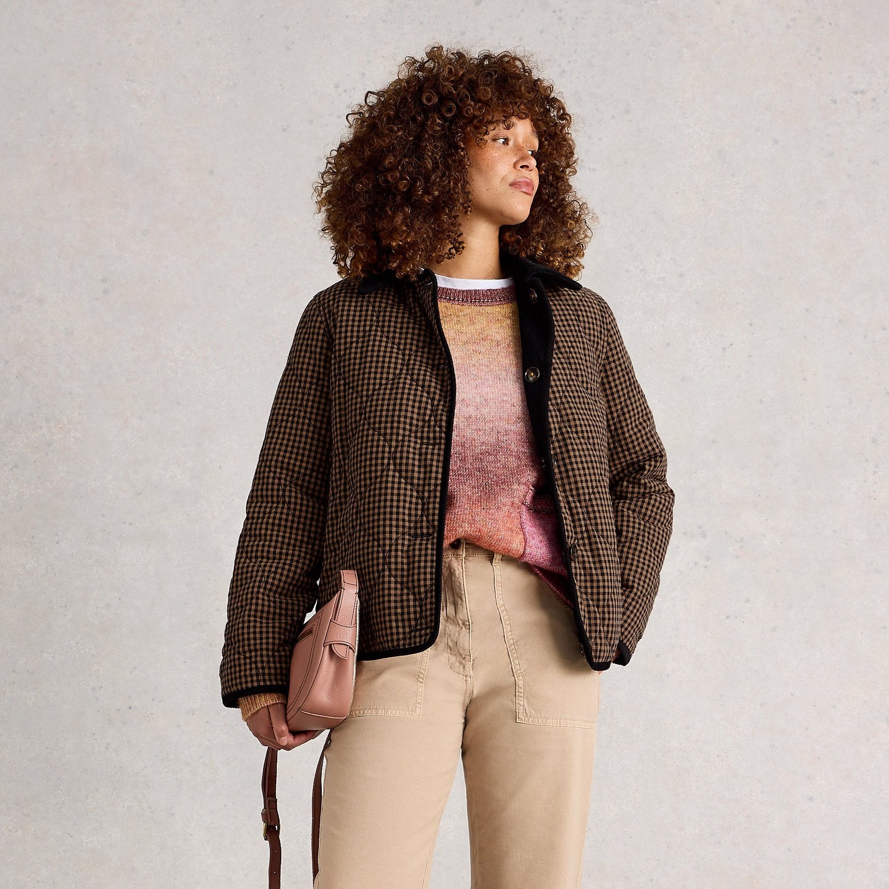 Woman wearing a brown checkered jacket, beige pants, and brown boots on a plain background