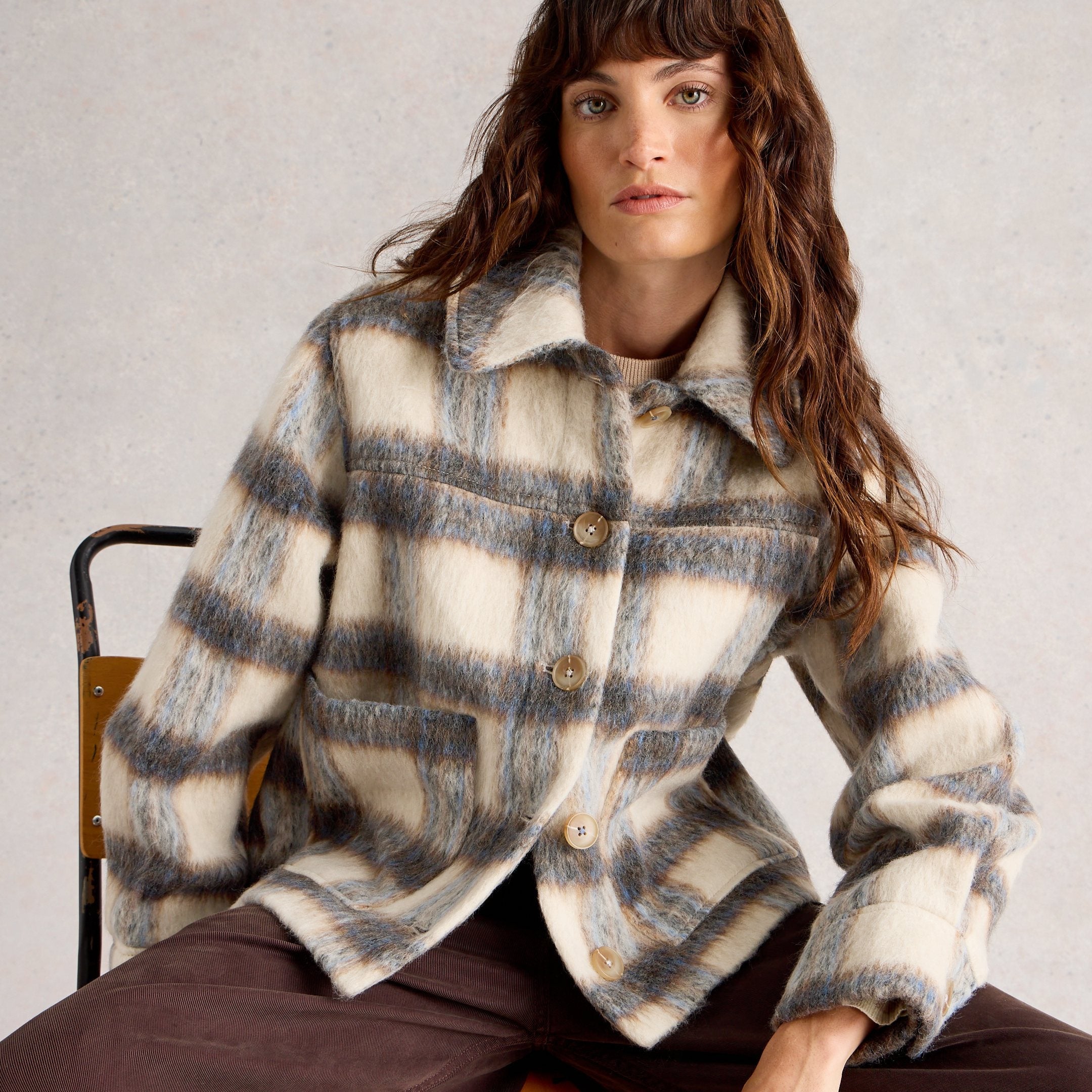 Woman wearing a plaid jacket sitting on a chair against a plain background