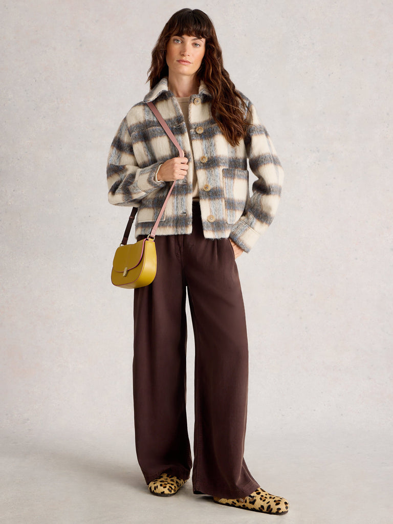 Woman wearing a plaid jacket and brown pants, holding a yellow handbag on a light gray background