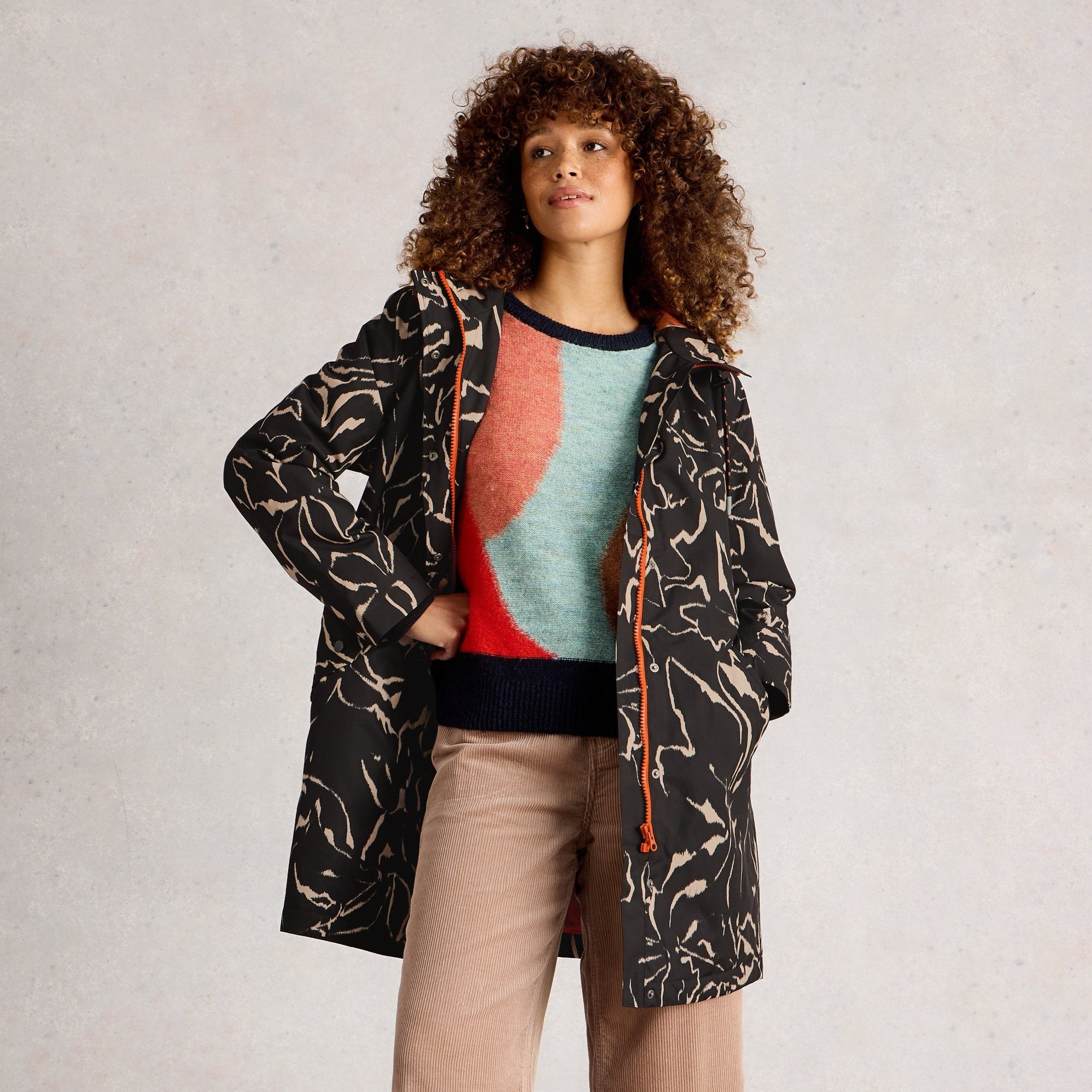 Woman wearing a patterned coat over a sweater and pants on a plain background